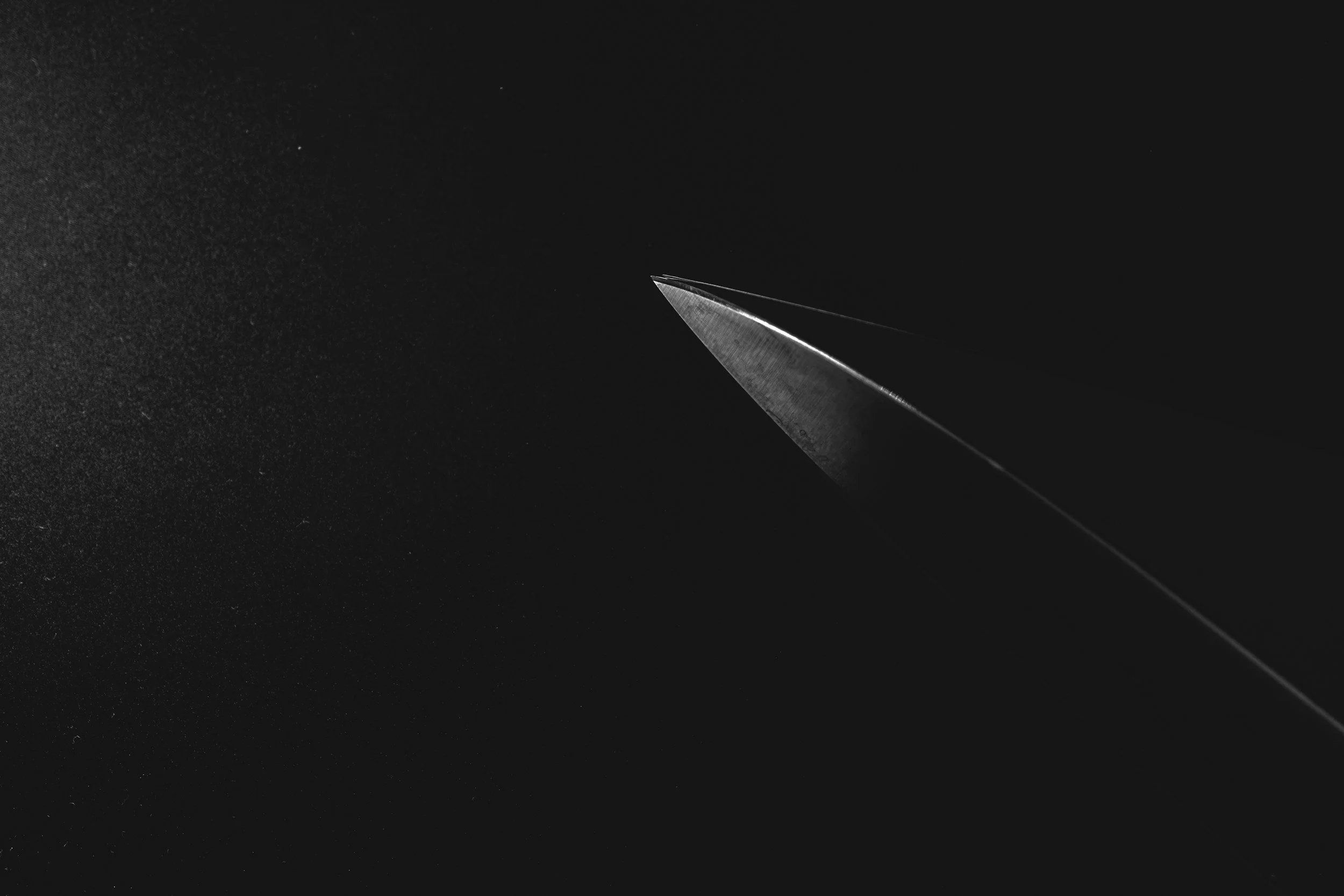 Close-up of a sharp blade pointed towards the dark background, with light reflecting off its edge.