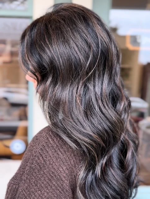 Side view of a woman with long, dark brown, wavy hair in a salon.