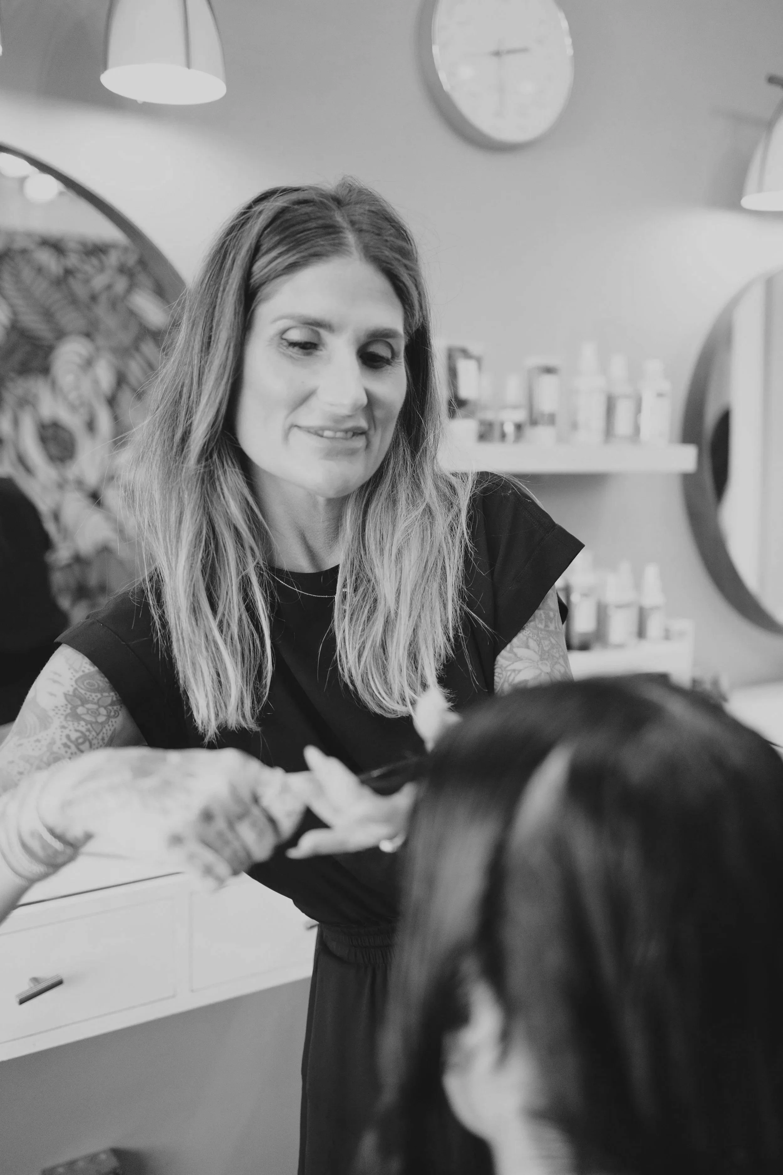 Tattooed woman with long hair smiling while holding a baby in a modern kitchen.
