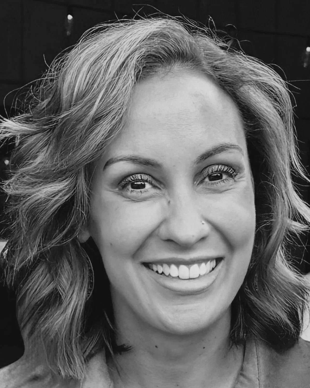 Black-and-white close-up portrait of a smiling woman with shoulder-length wavy hair