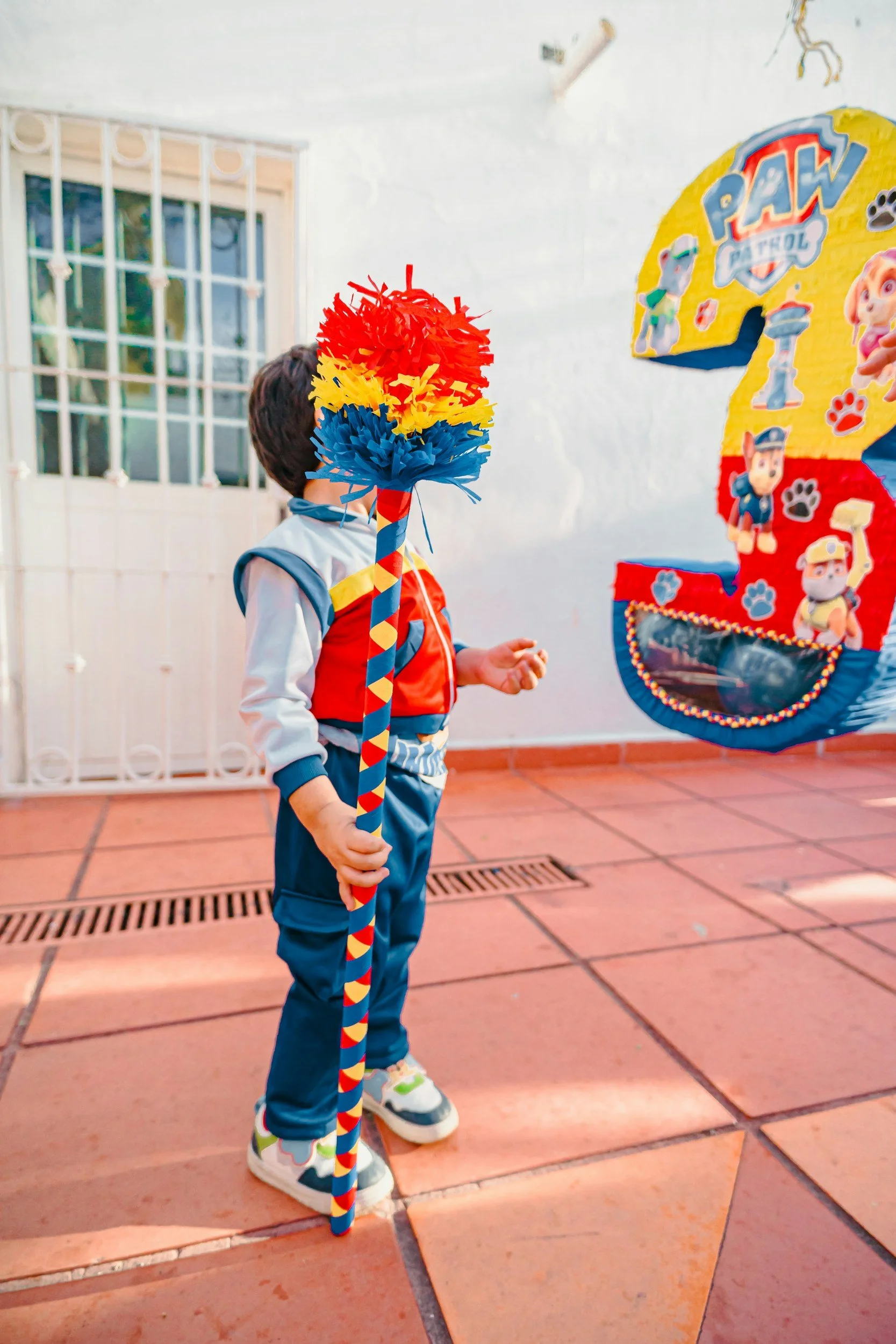 Child holding a colorful pinata stick at a birthday party with Paw Patrol themed decorations.