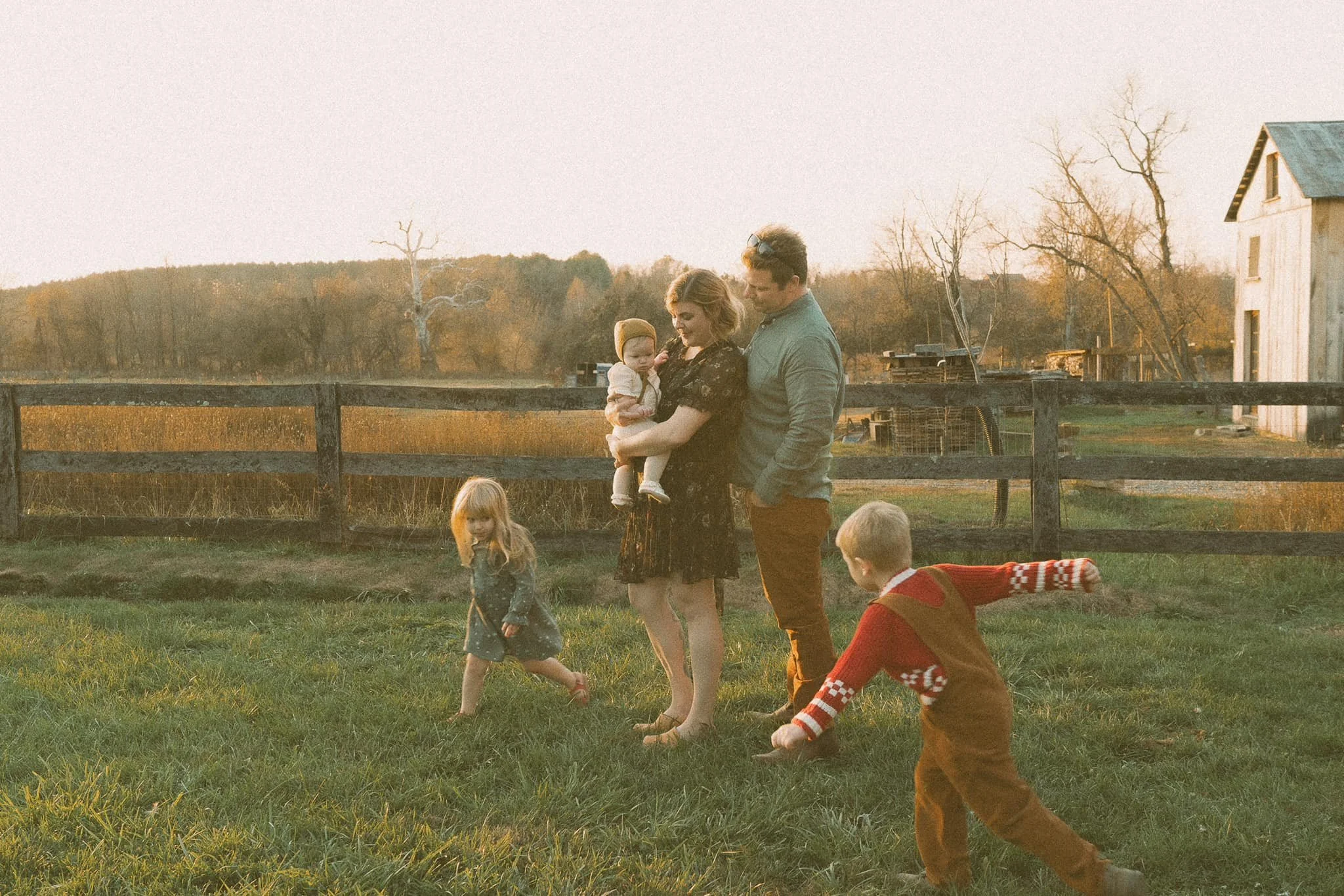 Family of five enjoying time outdoors on a grassy field during sunset, with trees and a fence in the background.