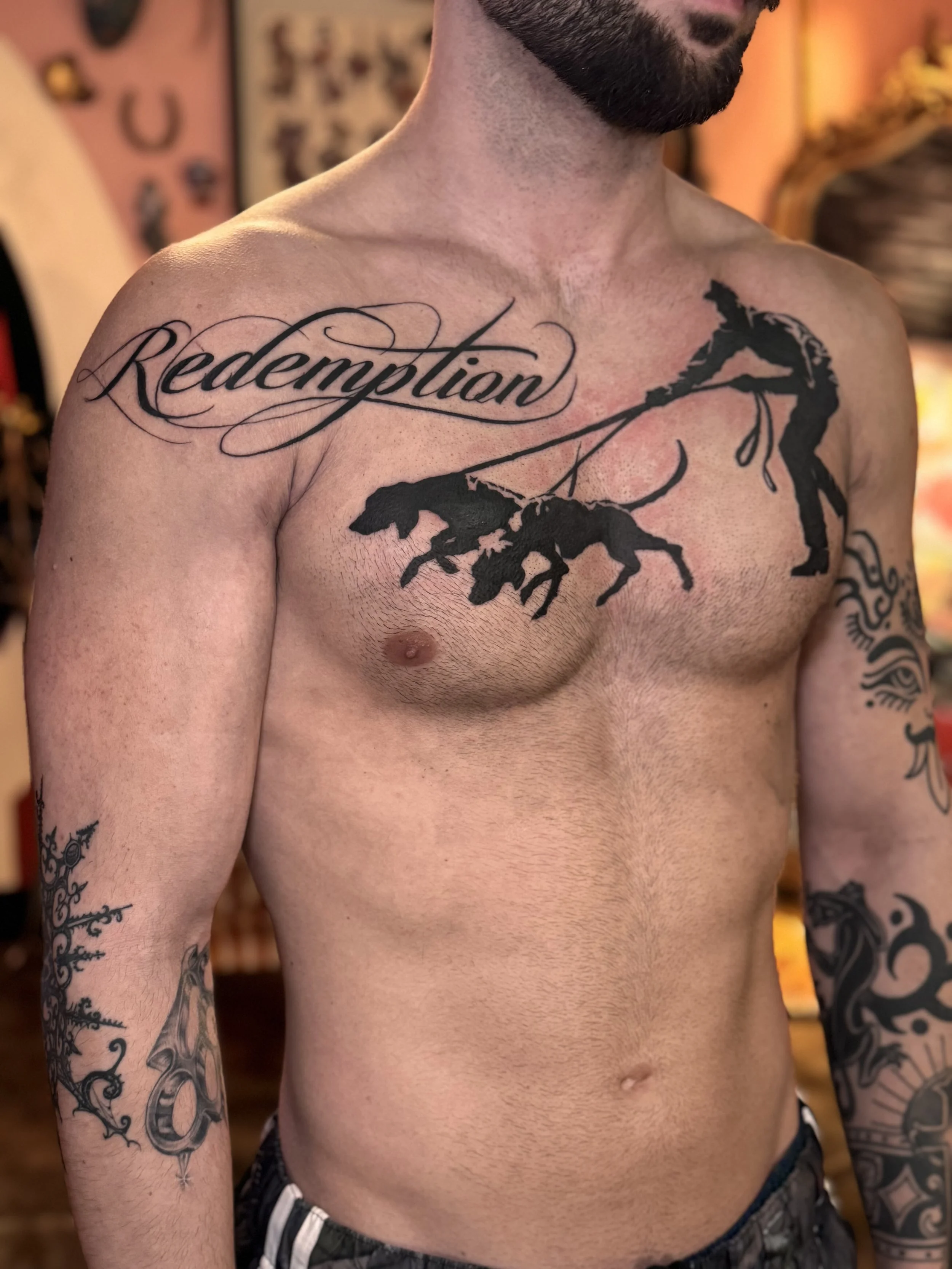 Lettering that says redemption in cursive across the chest next to a bansky tattoo