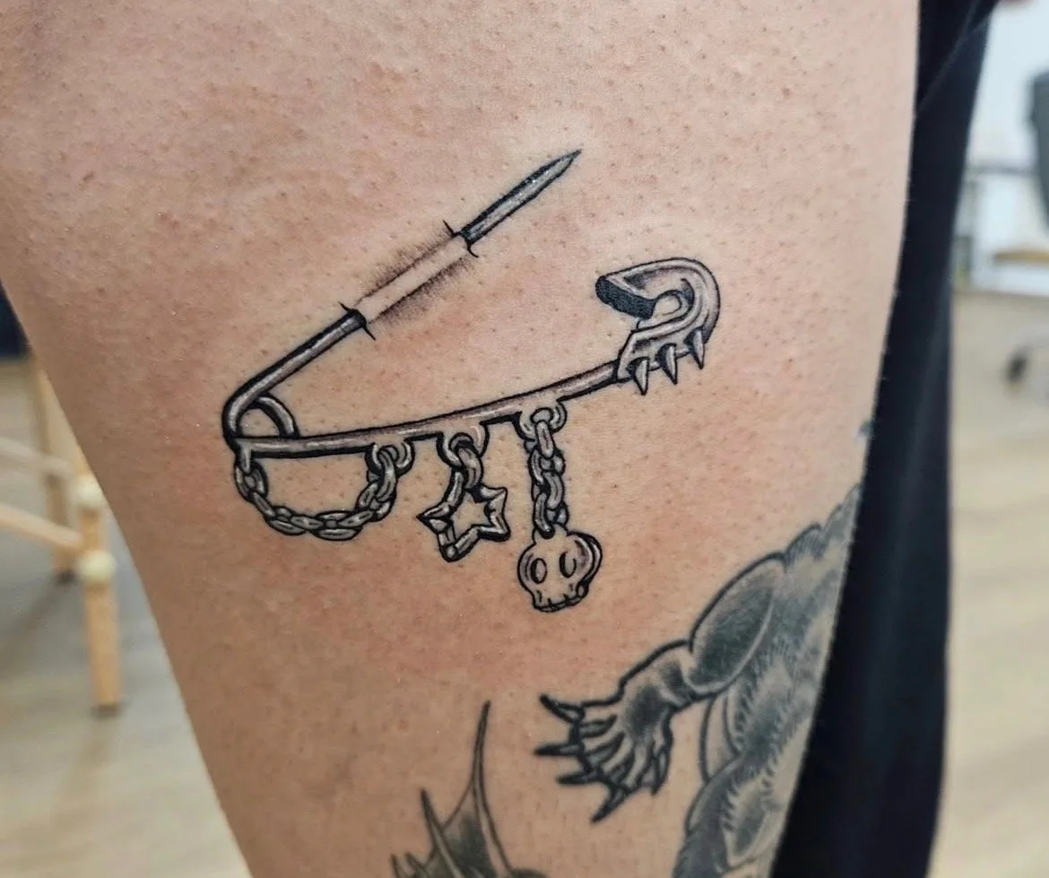 tiny black and grey  safety pin with charms tattoo 
