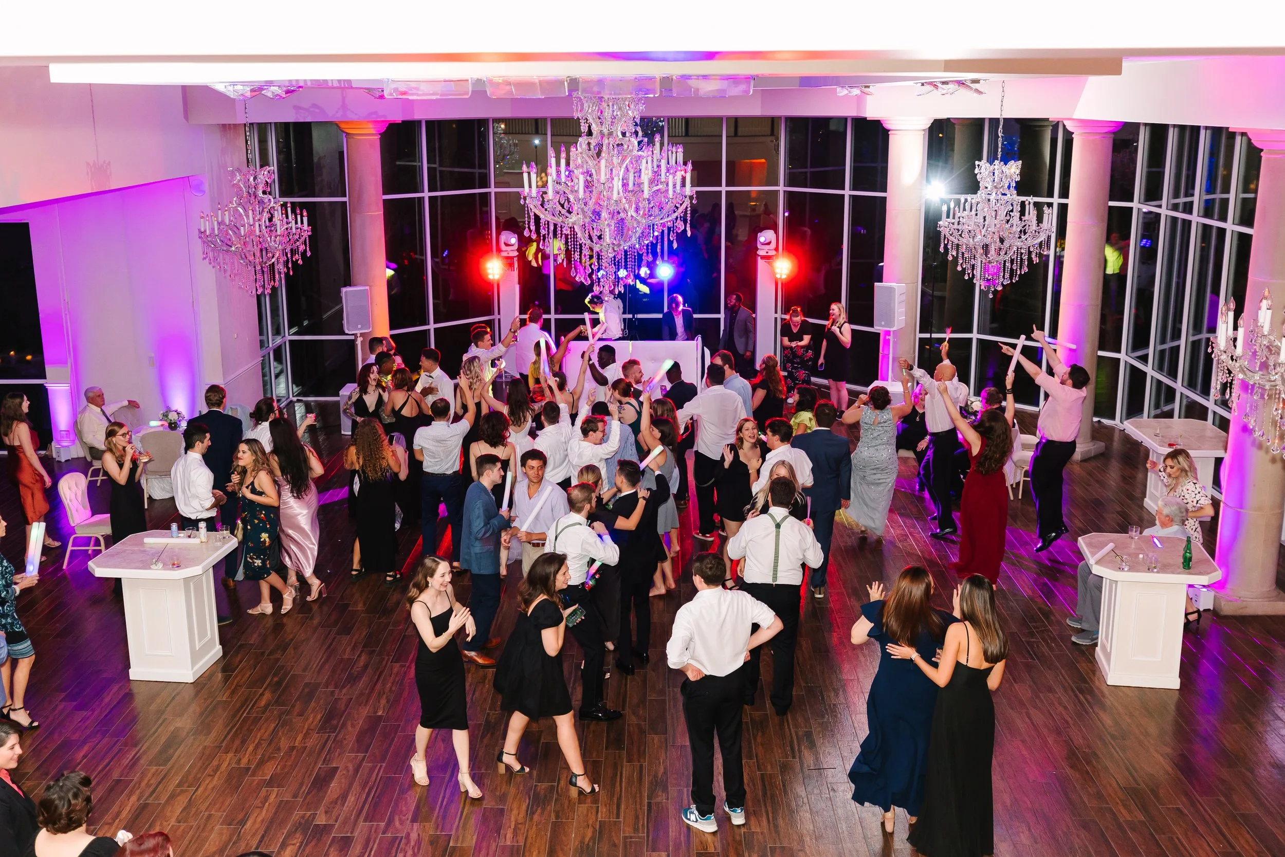 People dancing and enjoying music at a lively indoor party with large chandeliers and colorful lighting.