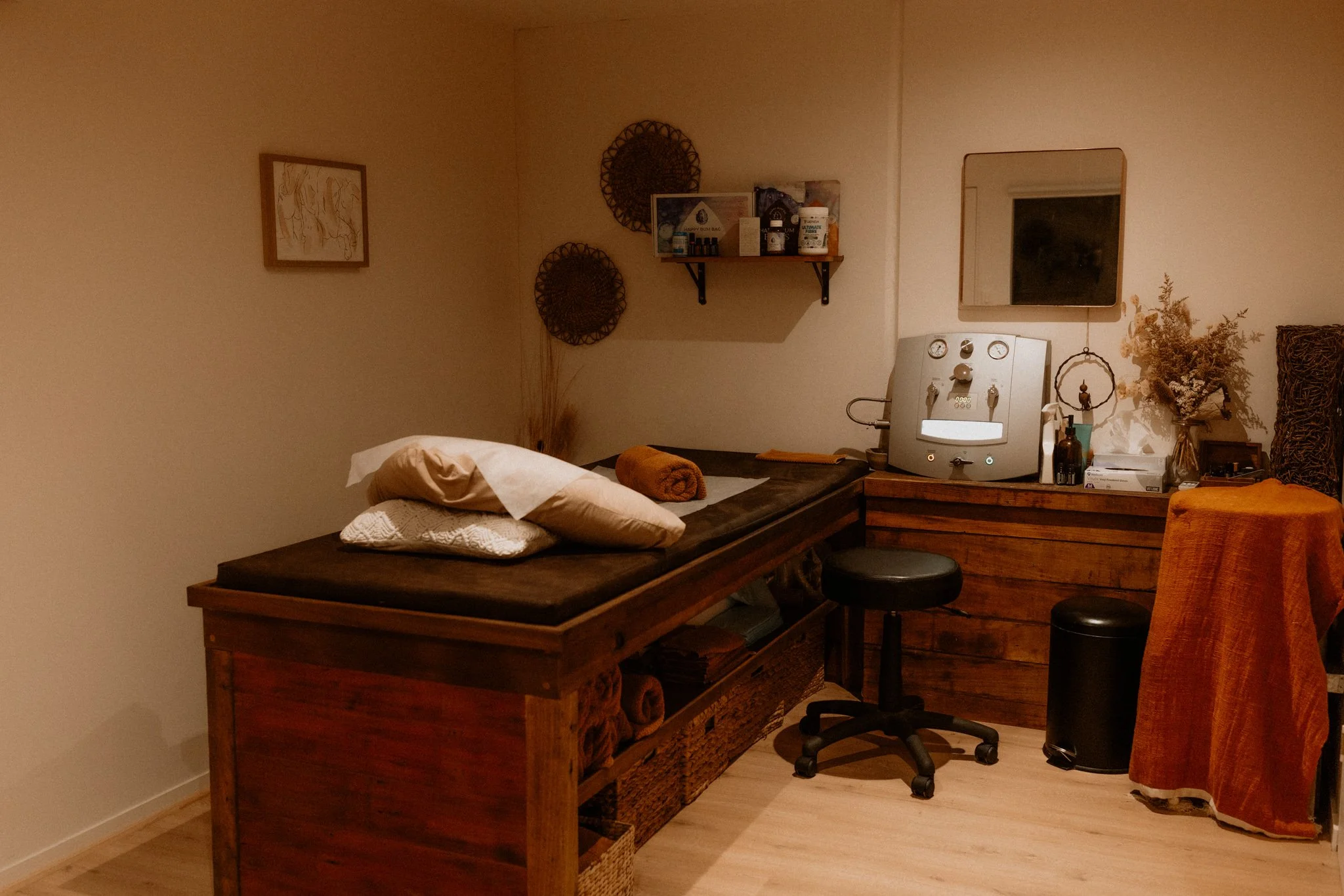 Flow Therapy treatment room with a warm, earthy aesthetic, treatment bed, colon hydrotherapy equipment, and calming decor.