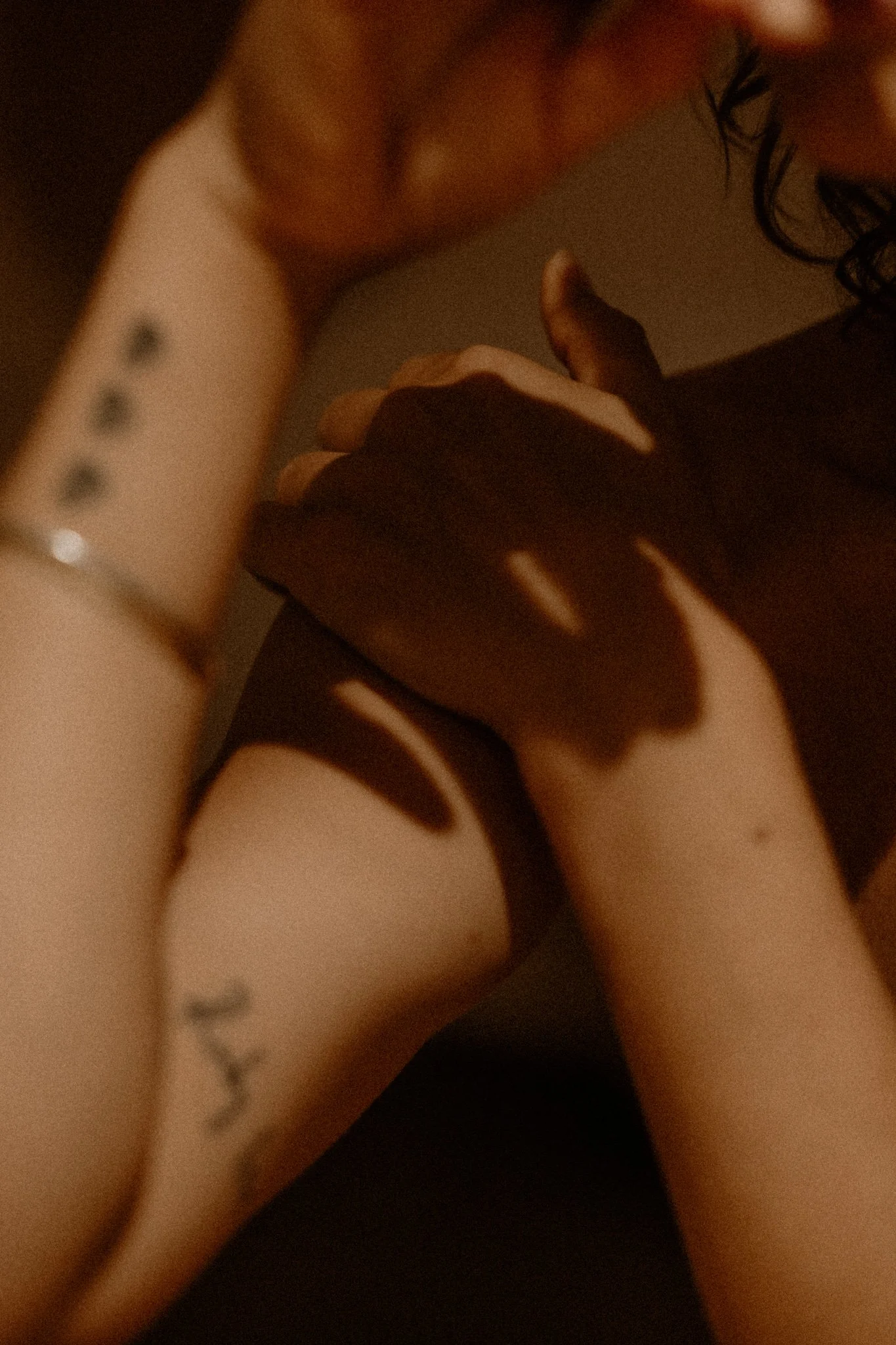 Close-up of a woman with curly hair touching her face and arm, with a shadow cast on her skin.