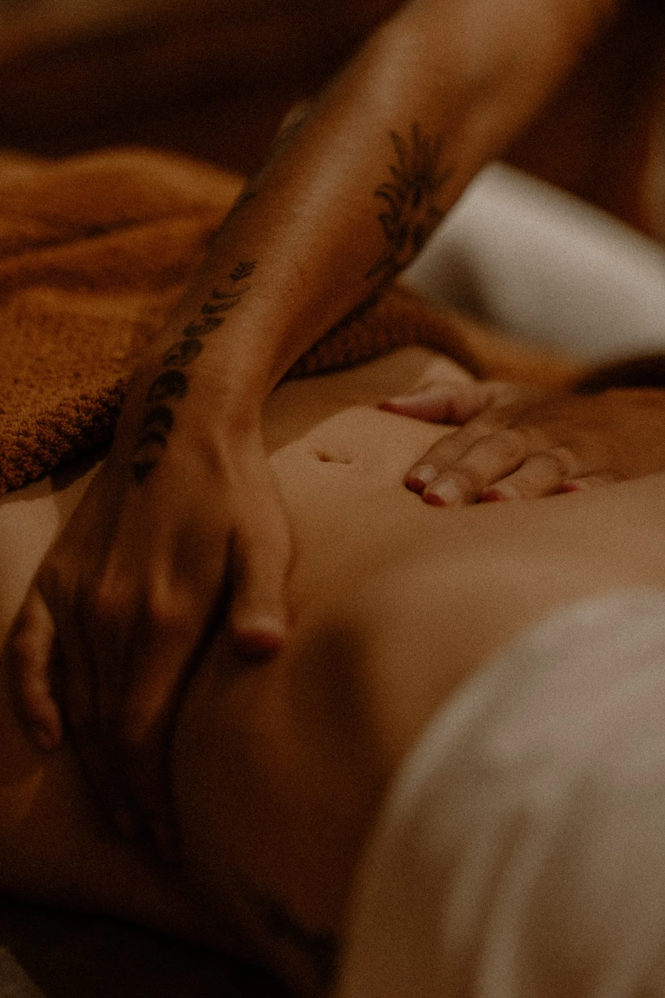 Close-up of a person receiving a massage, showing a hand with tattoos on the forearm applying pressure on a person's lower back.