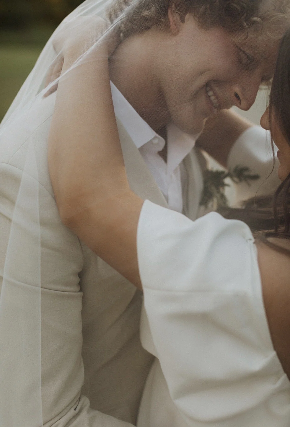 A man and woman close together, smiling and leaning in for a kiss at an outdoor setting.