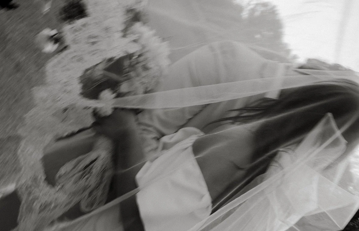 A woman in a wedding dress lying in a field of grass, partially covered by a transparent veil.