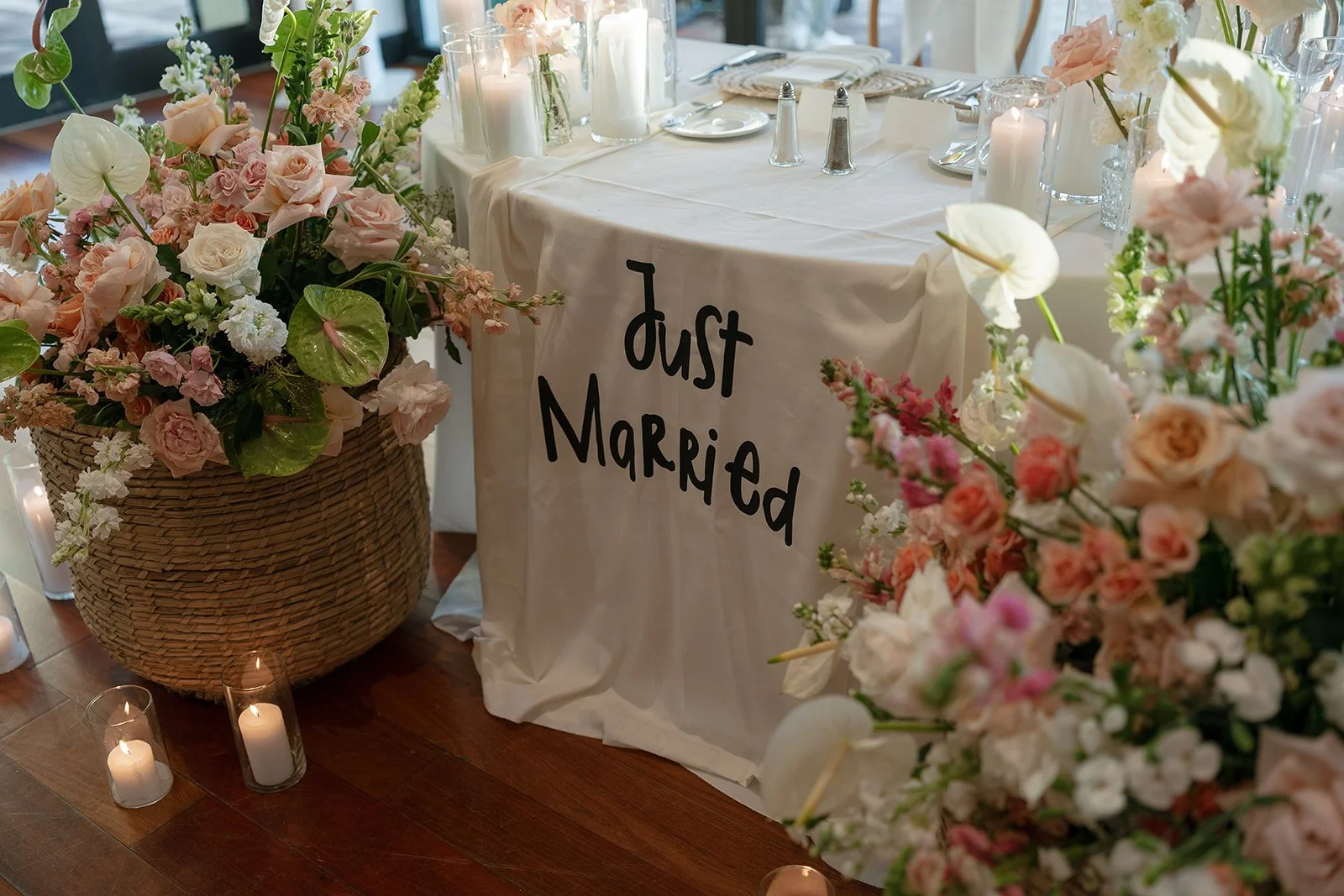 Wedding reception table with a white tablecloth, floral arrangements, candles, and a sign that says 'Just Married'.