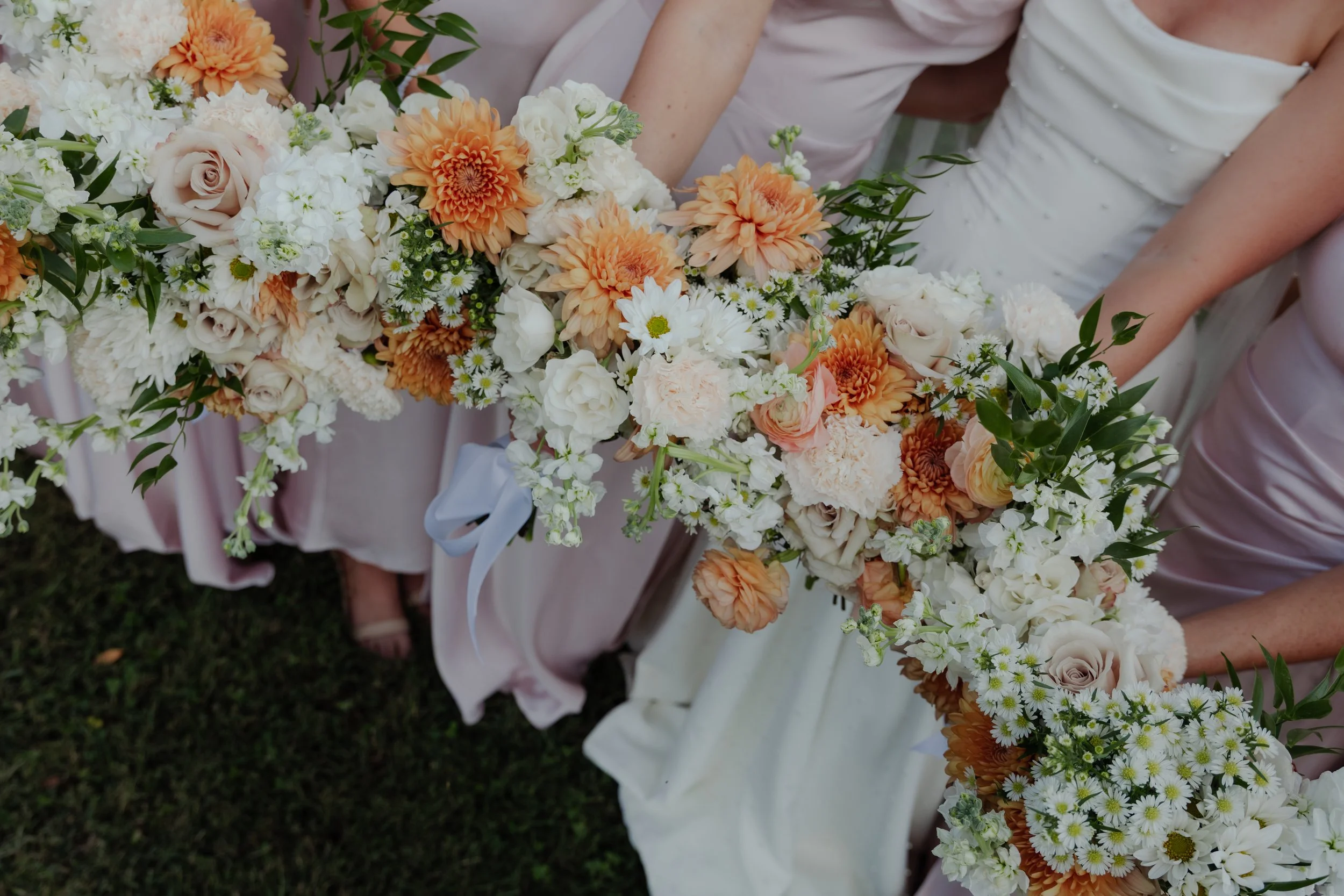 Wedding party holding a long, cascading floral arrangement with peach, white, and cream-colored flowers and greenery.
