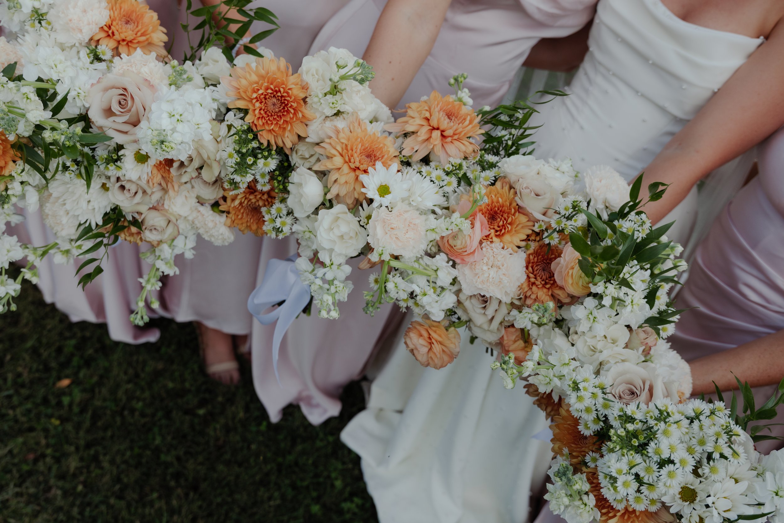 Bridesmaids holding a long, cascading floral bouquet with peach, white, and cream-colored flowers and greenery at a wedding.