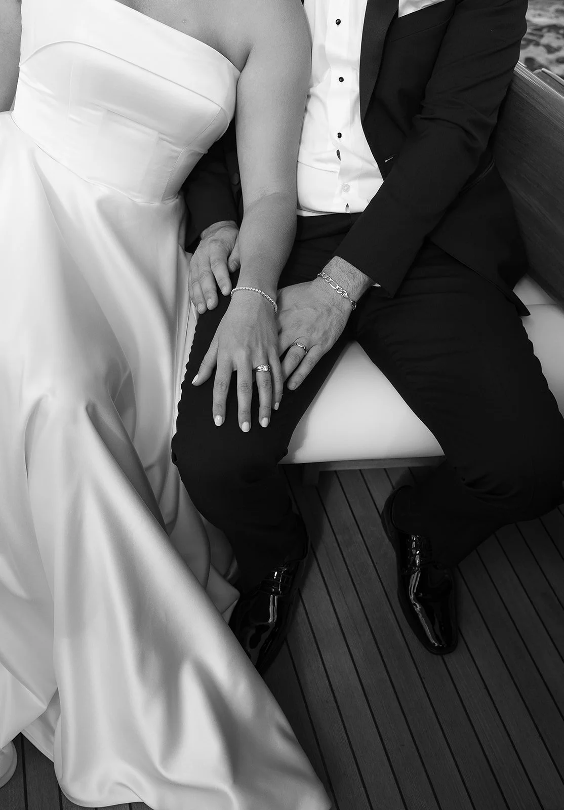 Black and white photo of a bride and groom with their hands resting on each other, showing wedding rings.