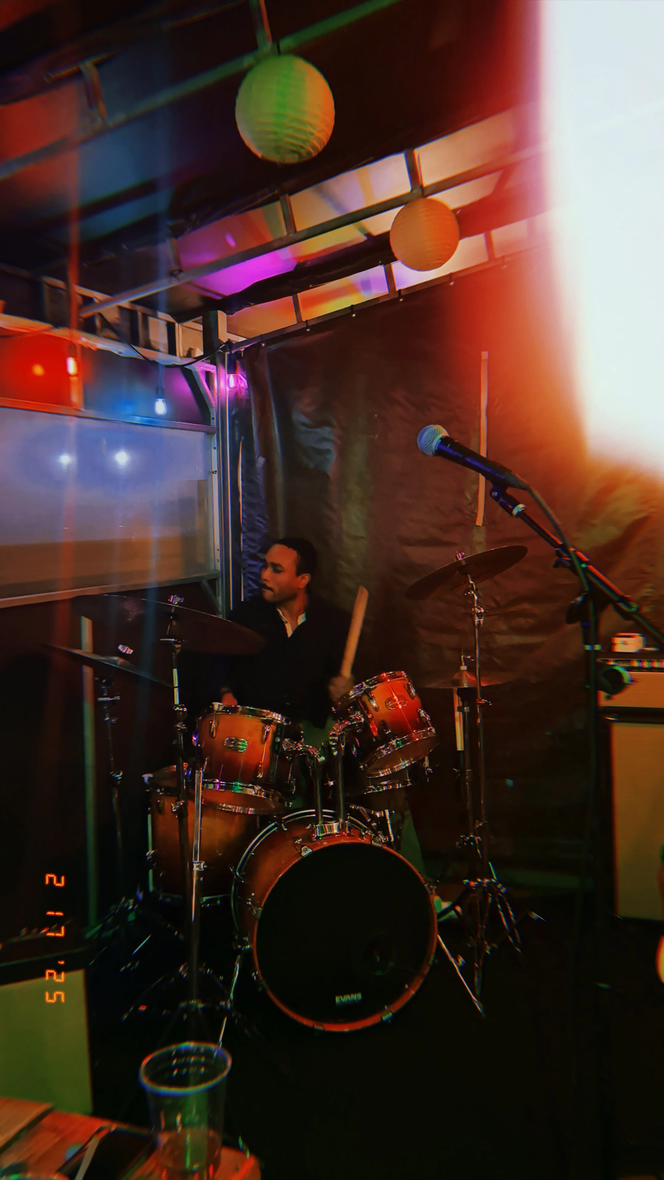 A person playing drums on stage with colorful lights and paper lanterns hanging from the ceiling.