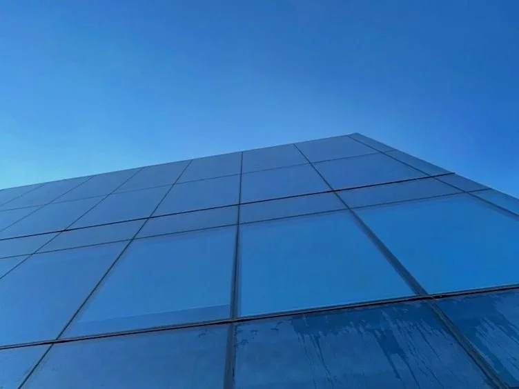 Looking up at a modern glass building against a clear blue sky.