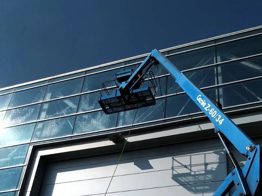 A blue cherry picker lifting workers to clean or maintain the exterior glass windows of a modern building.