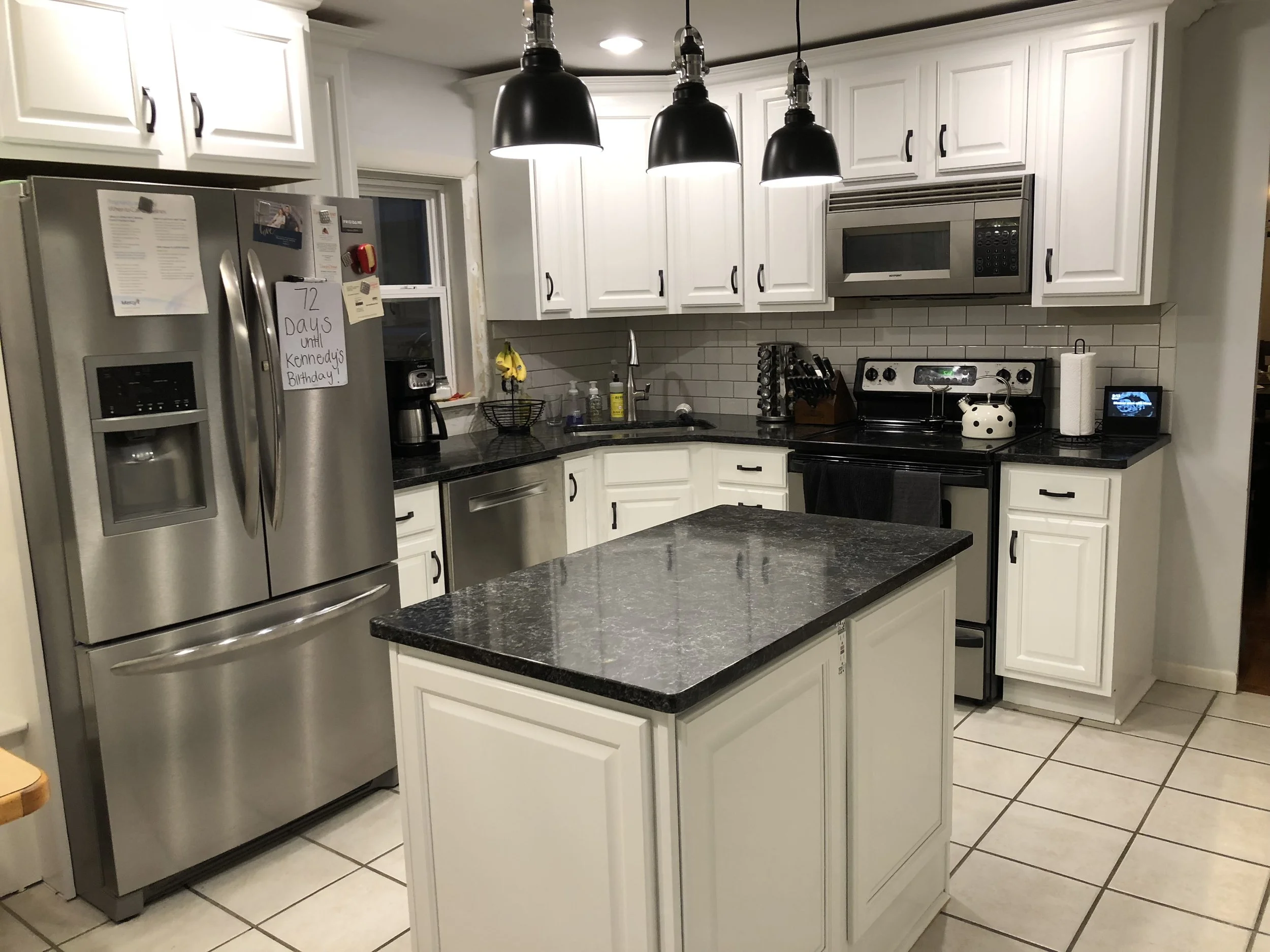 Kitchen with white cabinets, black countertops, a refrigerator with notes, a microwave, oven, and island with a black top.