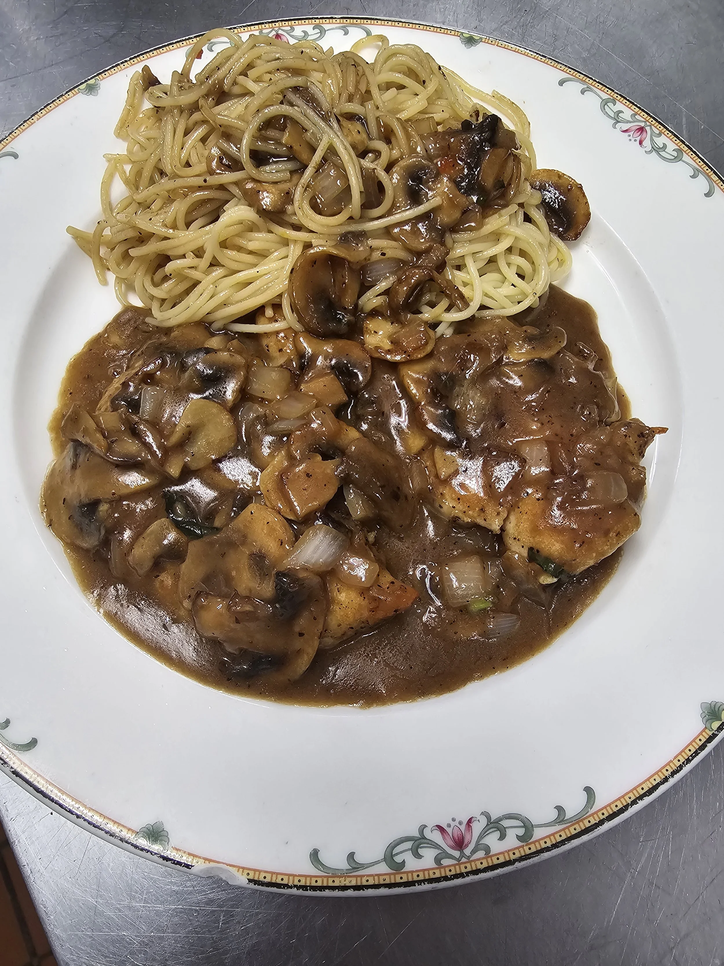 Plate of chicken with mushroom sauce and side of spaghetti with mushrooms.