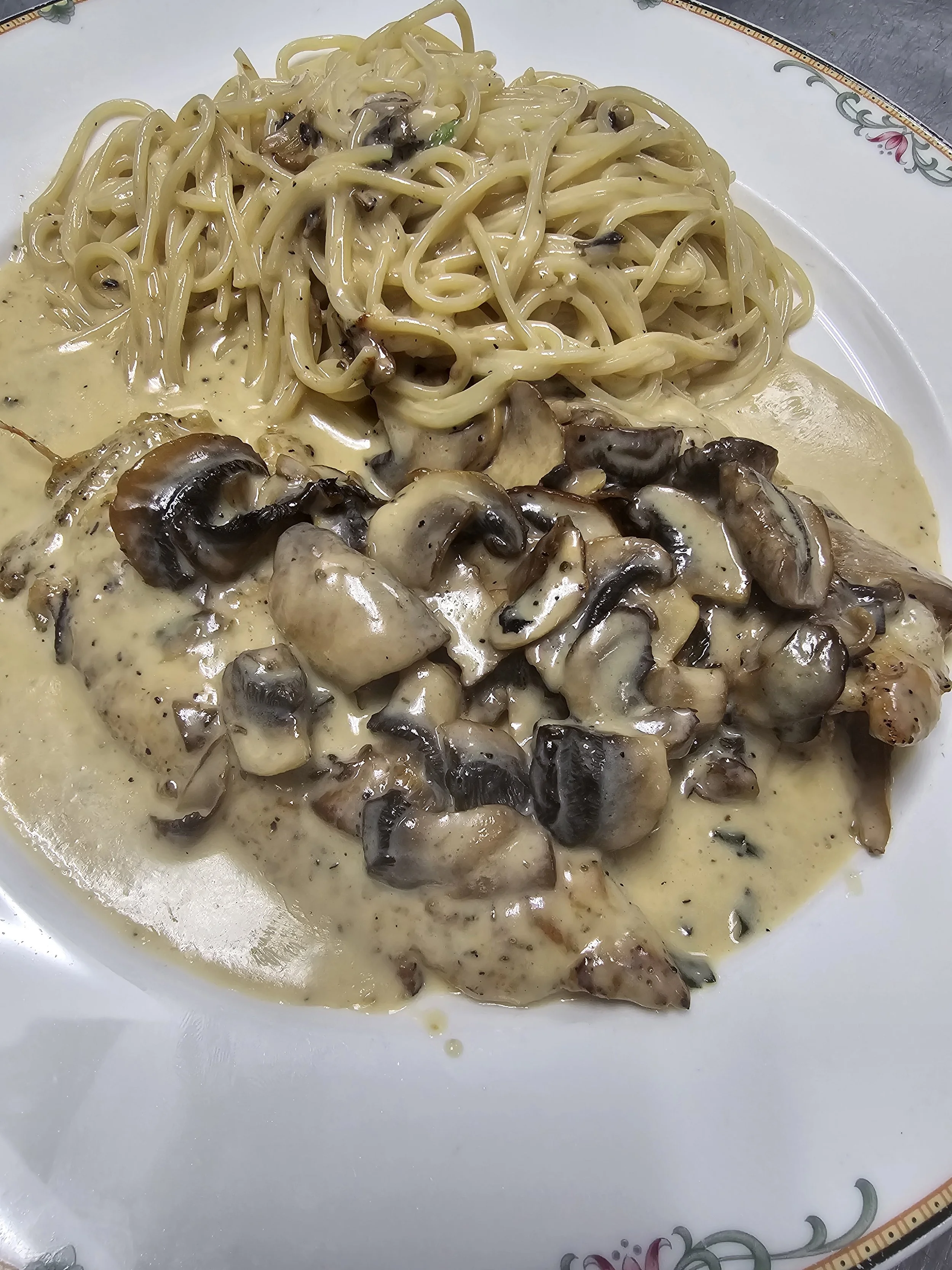 Plate of chicken with mushroom cream sauce and cooked spaghetti.