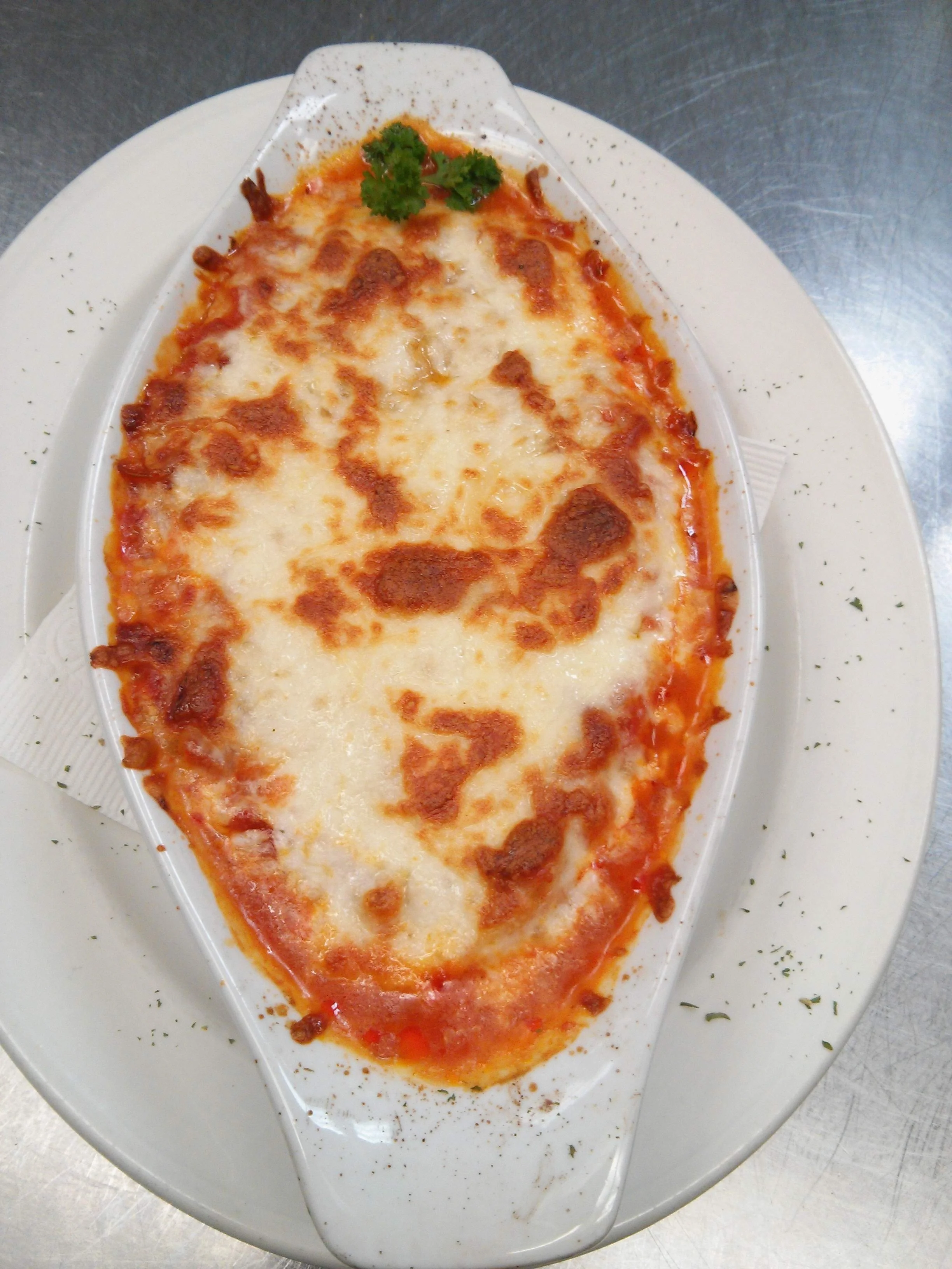 Baked pizza with melted cheese and a sprig of parsley served on a white dish