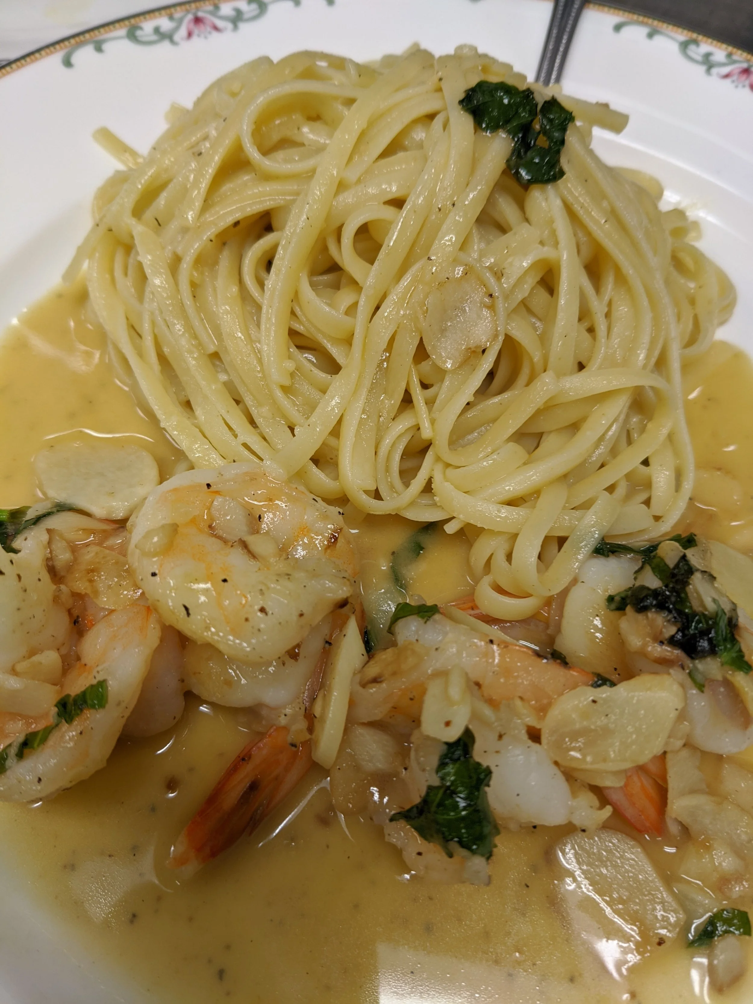 Plate of cooked spaghetti topped with herbs and garlic, served with shrimp and a creamy sauce with garlic slices.