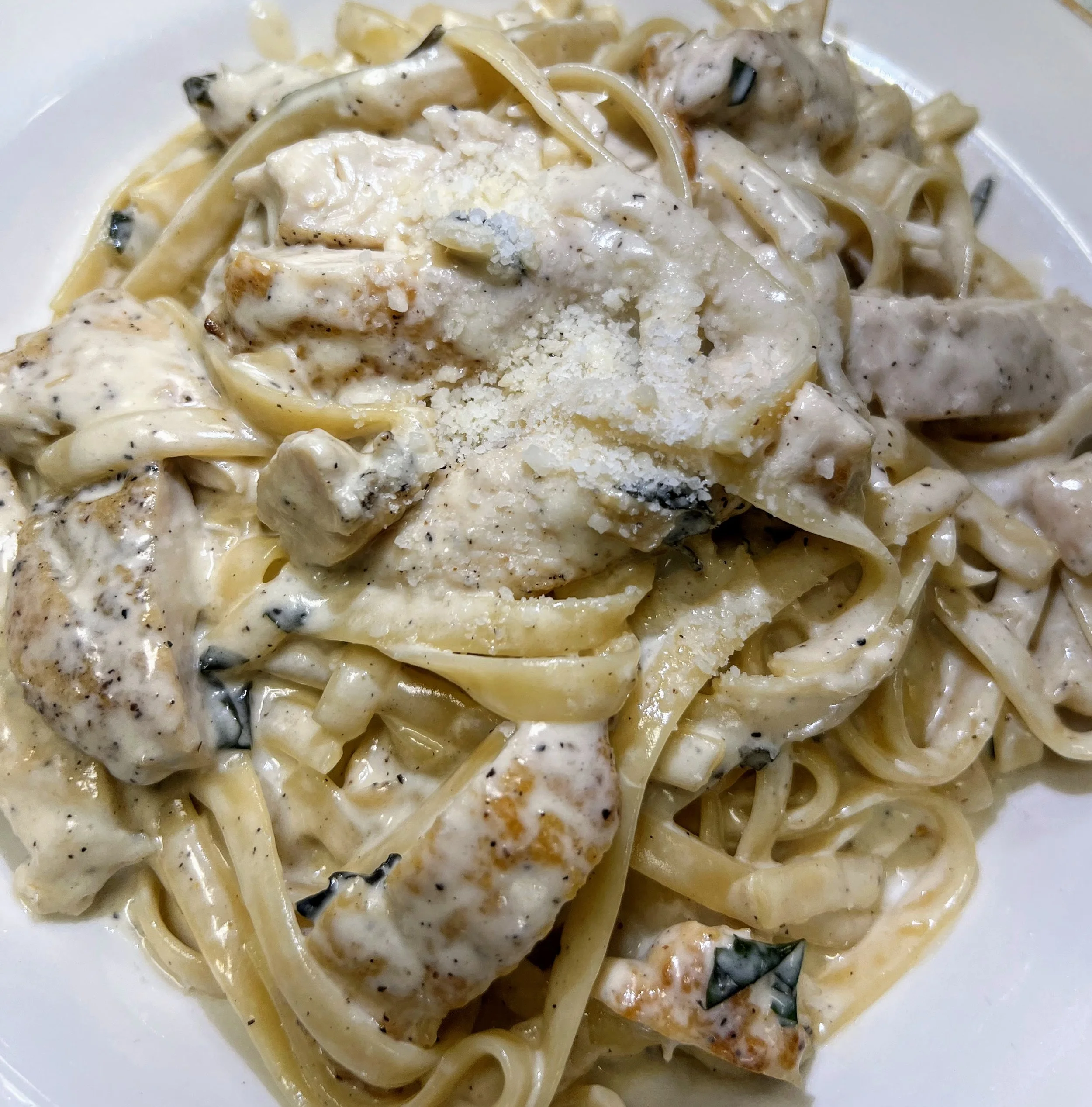 Close-up of a plate of creamy chicken Alfredo pasta with fettuccine, chunks of chicken, and grated cheese.