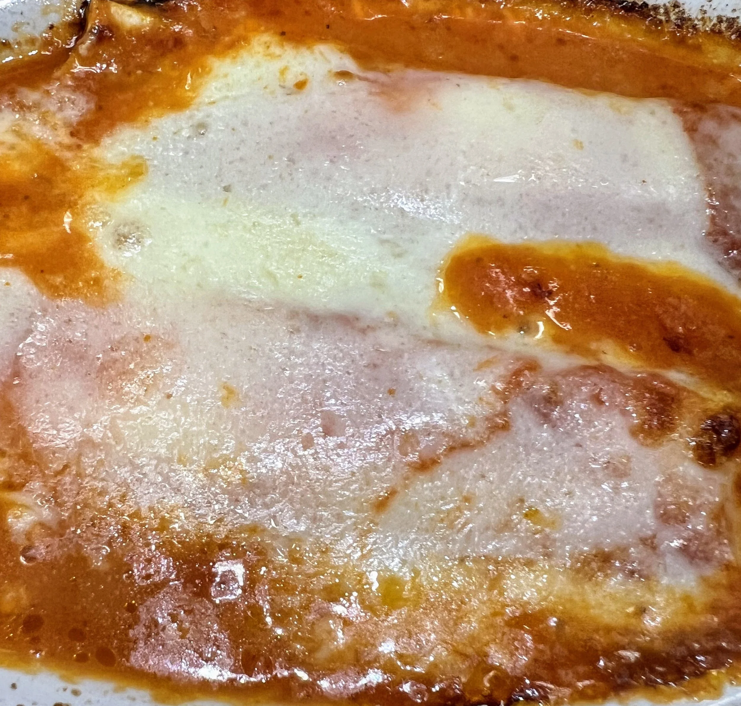 Close-up of a baked dish with melted cheese and tomato sauce.