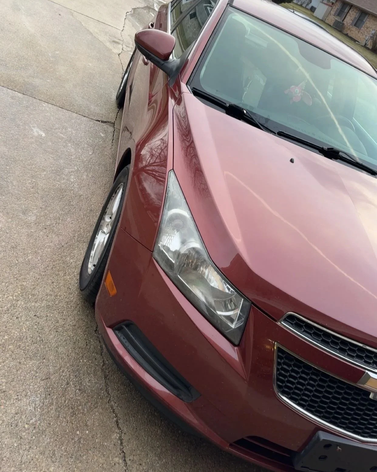 A red Chevrolet sedan parked on a concrete driveway with a house and trees visible in the background.