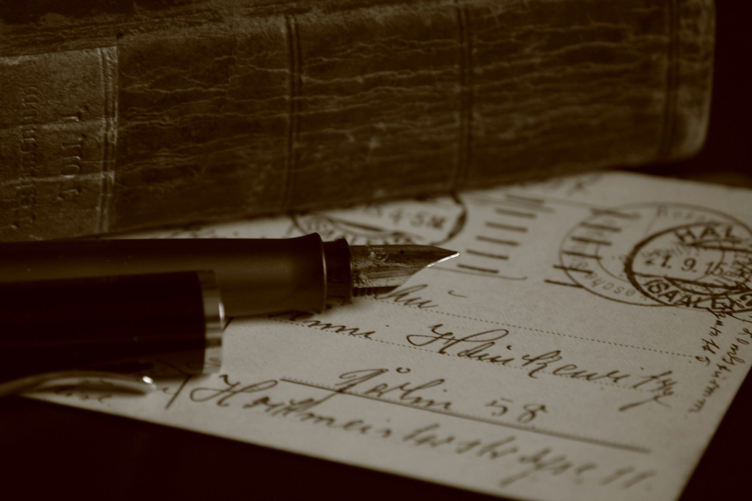 Close-up of a fountain pen resting on handwritten letter paper with a vintage postmark, and a wooden ink stand in the background.