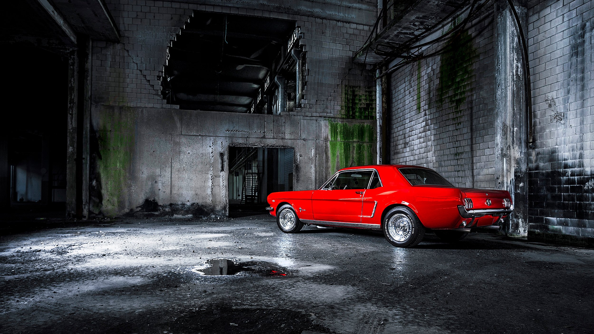 Roter klassischer Auto in einer verfallenen Industriehalle, halb im Schatten, mit Wasserpfütze auf dem Boden.