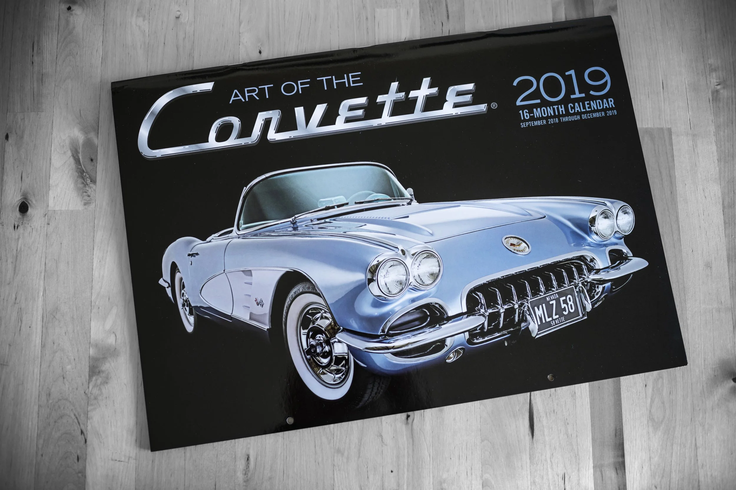 Ein kalender mit dem Titel 'Art of the Corvette 2019', der ein Bild eines weißen Corvettes zeigt, liegt auf einem Holzboden.