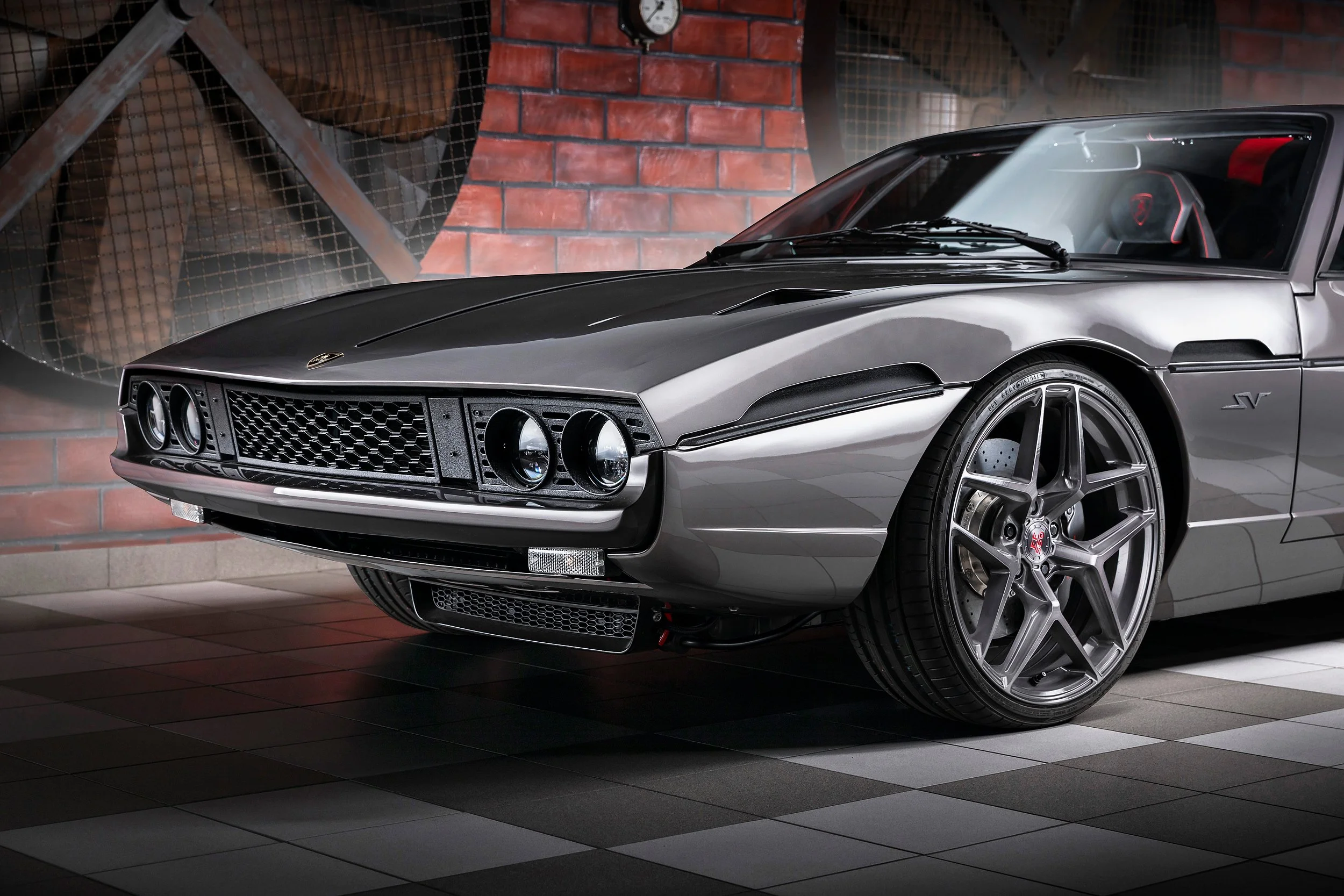 Ein silberner Ferrari Sportwagen in einer Autowerkstatt, vor einer Wand aus roten Ziegelsteinen.