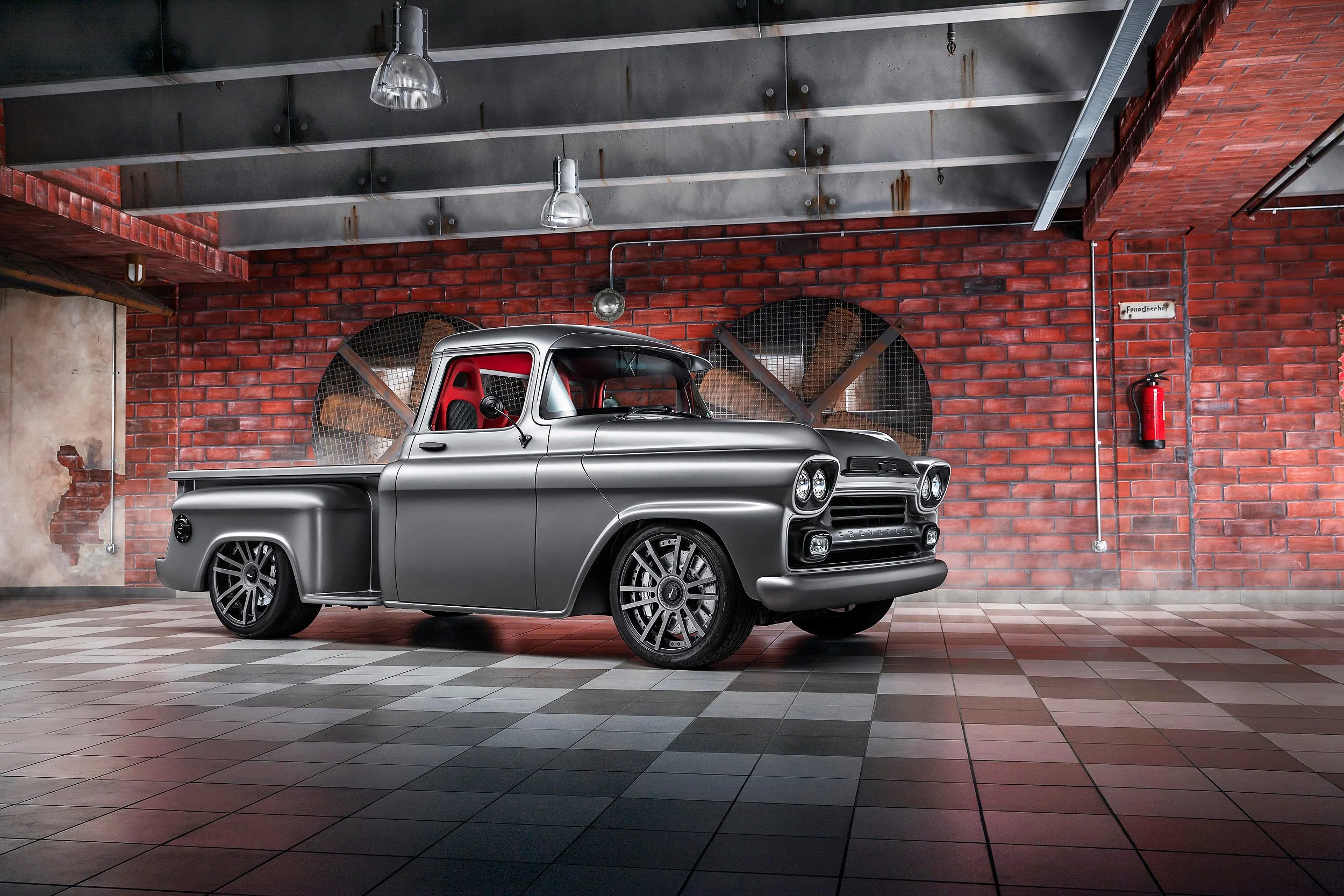 Ein silberner Oldtimer-Pickup in einer industriellen Garage mit roten Ziegelwänden, Fliesenboden und industriellem Deckenlicht.