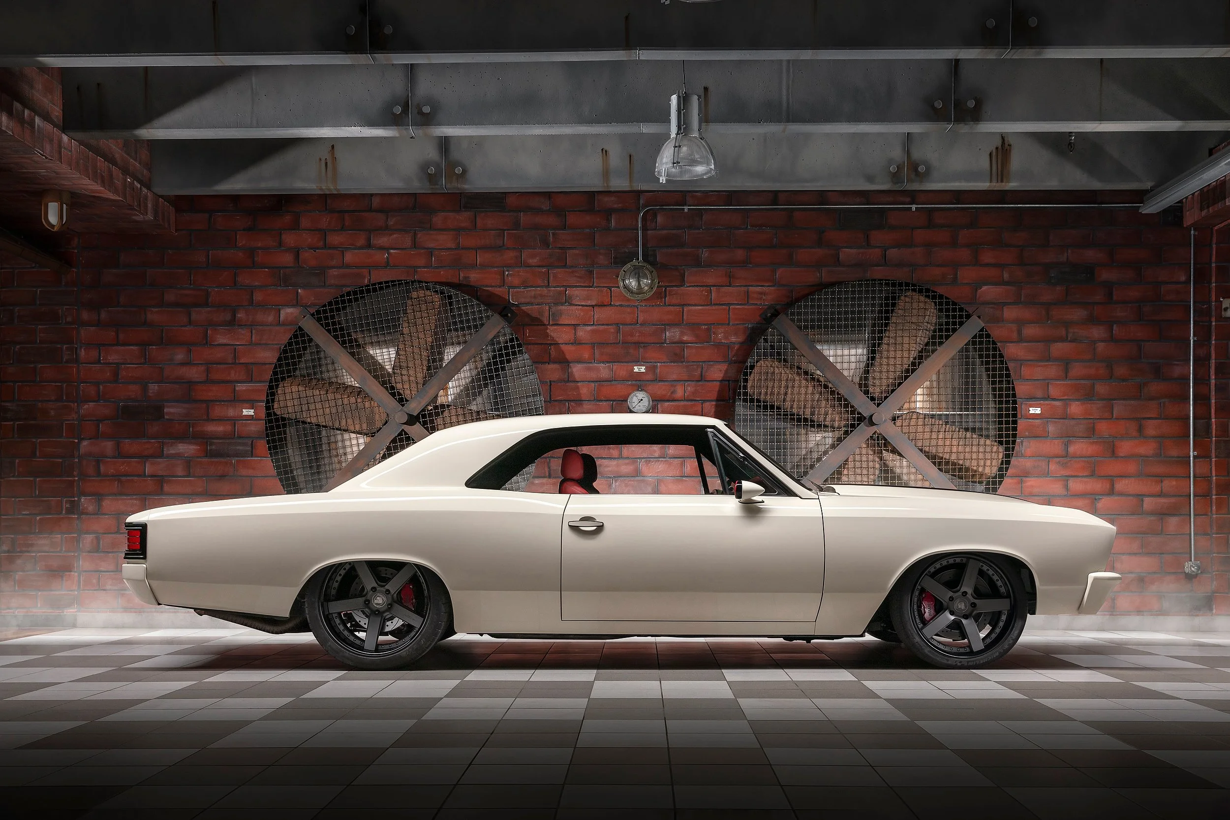 Ein weißer Oldtimer-Auto steht in einer Garage mit roten Ziegelwänden und grauem Fliesenboden.