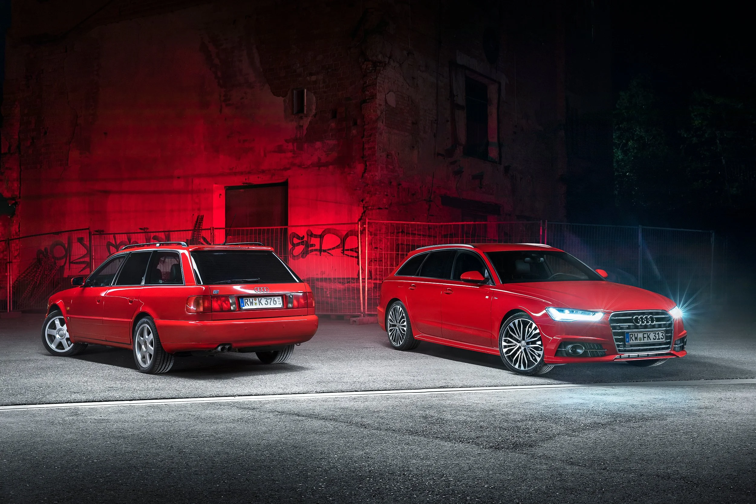 Zwei rote Autos, ein Kombi und ein Limousine, parken vor einer alten, beschädigten Steinmauer mit Graffiti bei Nacht.