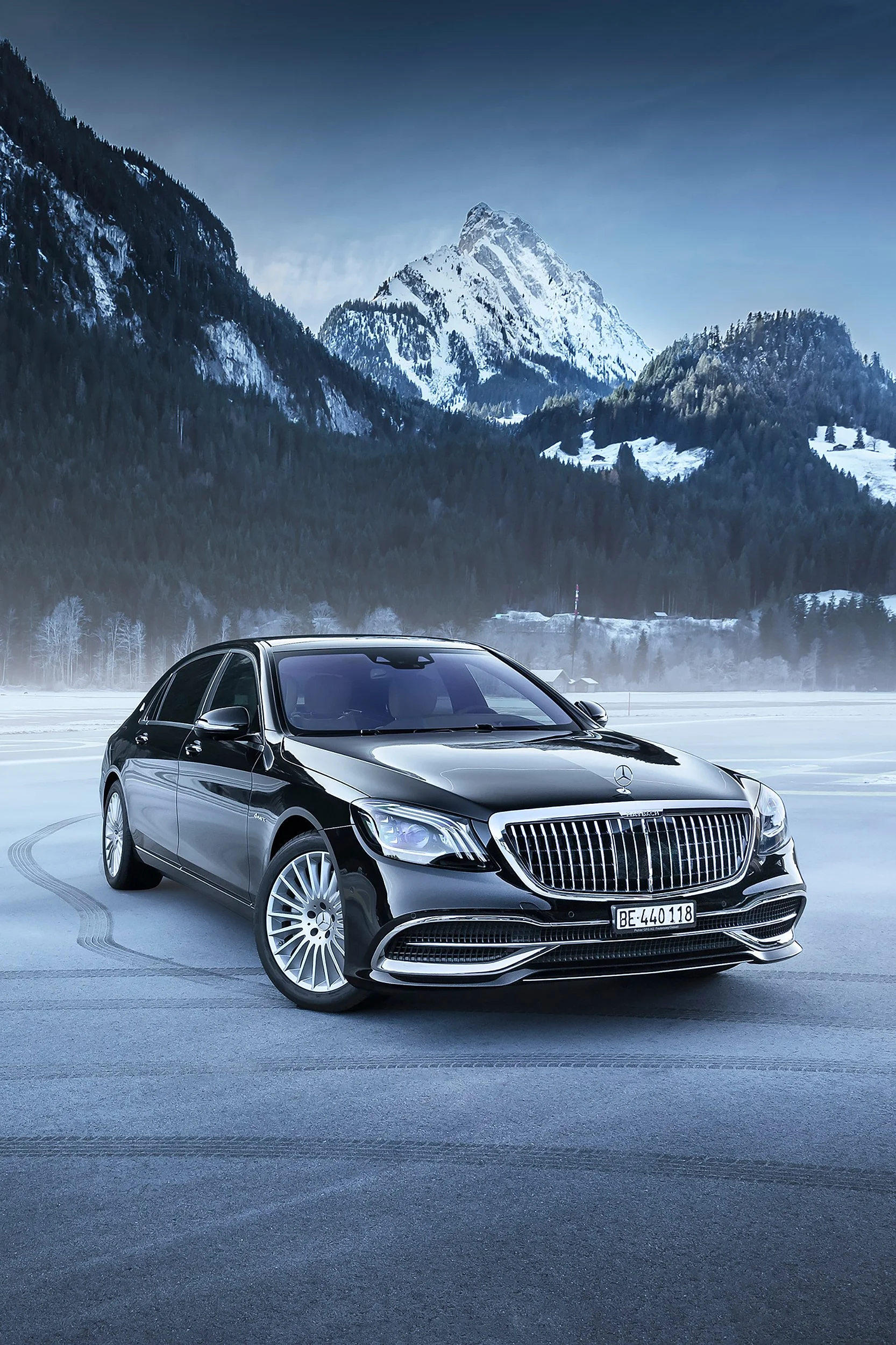 Ein schwarzer Mercedes-Benz Limousine auf einer Winter-Straßenbahn, im Hintergrund verschneite Berge und eine bewölkte Himmel.