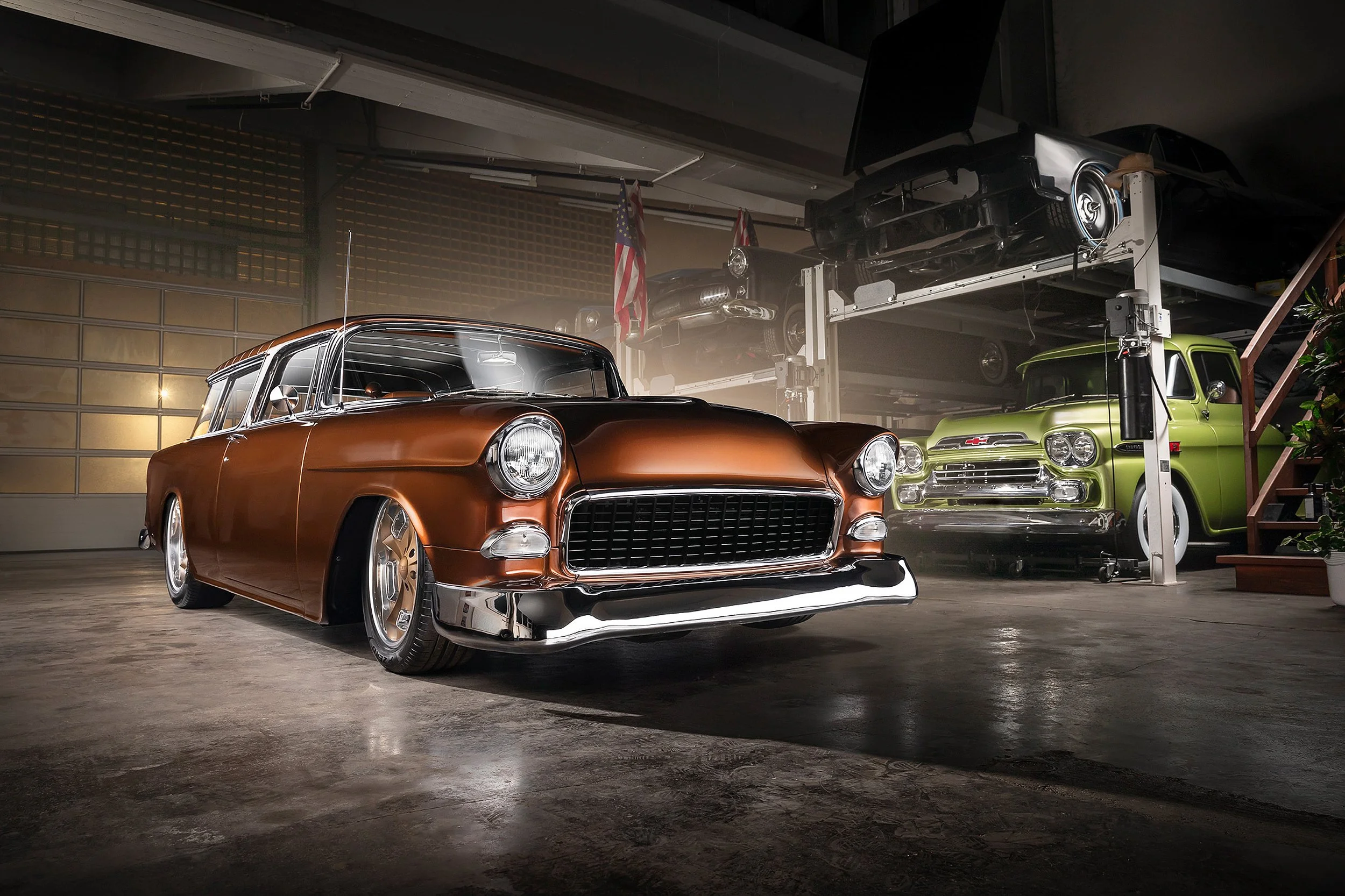Ein Oldtimer-Parkhaus mit mehreren Autos, darunter ein schwarzer und ein grüner Chevrolet, in einer Garage mit Betonboden und einem Regal mit weiteren Fahrzeugen im oberen Bereich.