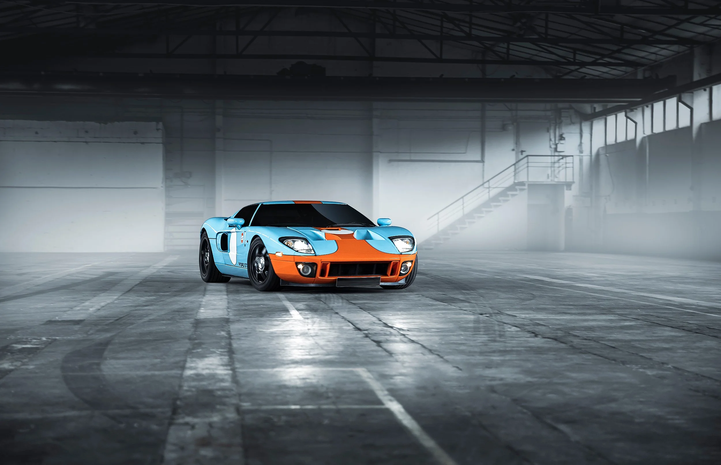 Ein sportwagen in einem Industriehallen mit gedämpfter Beleuchtung, hauptsächlich in blau und orangefarben, steht auf einer weißen Markierung auf dem Boden.