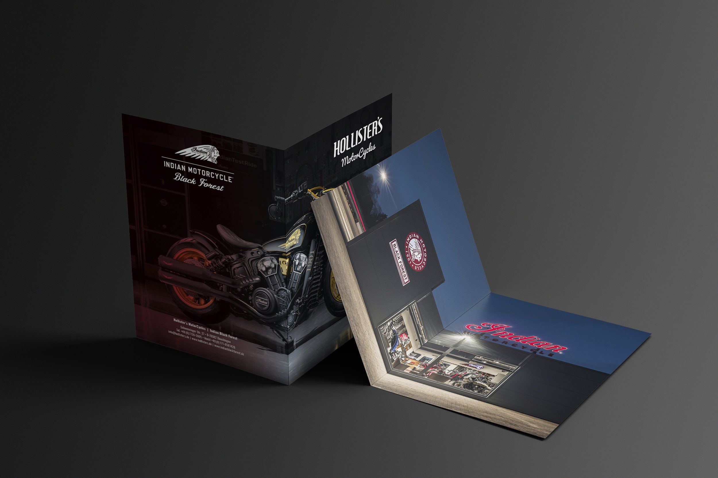 Drei aufklappbare Poster stehen auf einer dunklen Oberfläche. Die Poster zeigen Marken und Bilder von Motorrädern und Motorradzubehör, darunter Indian Motorcycle, Harley-Davidson, und Hollister's Motor Cycles.