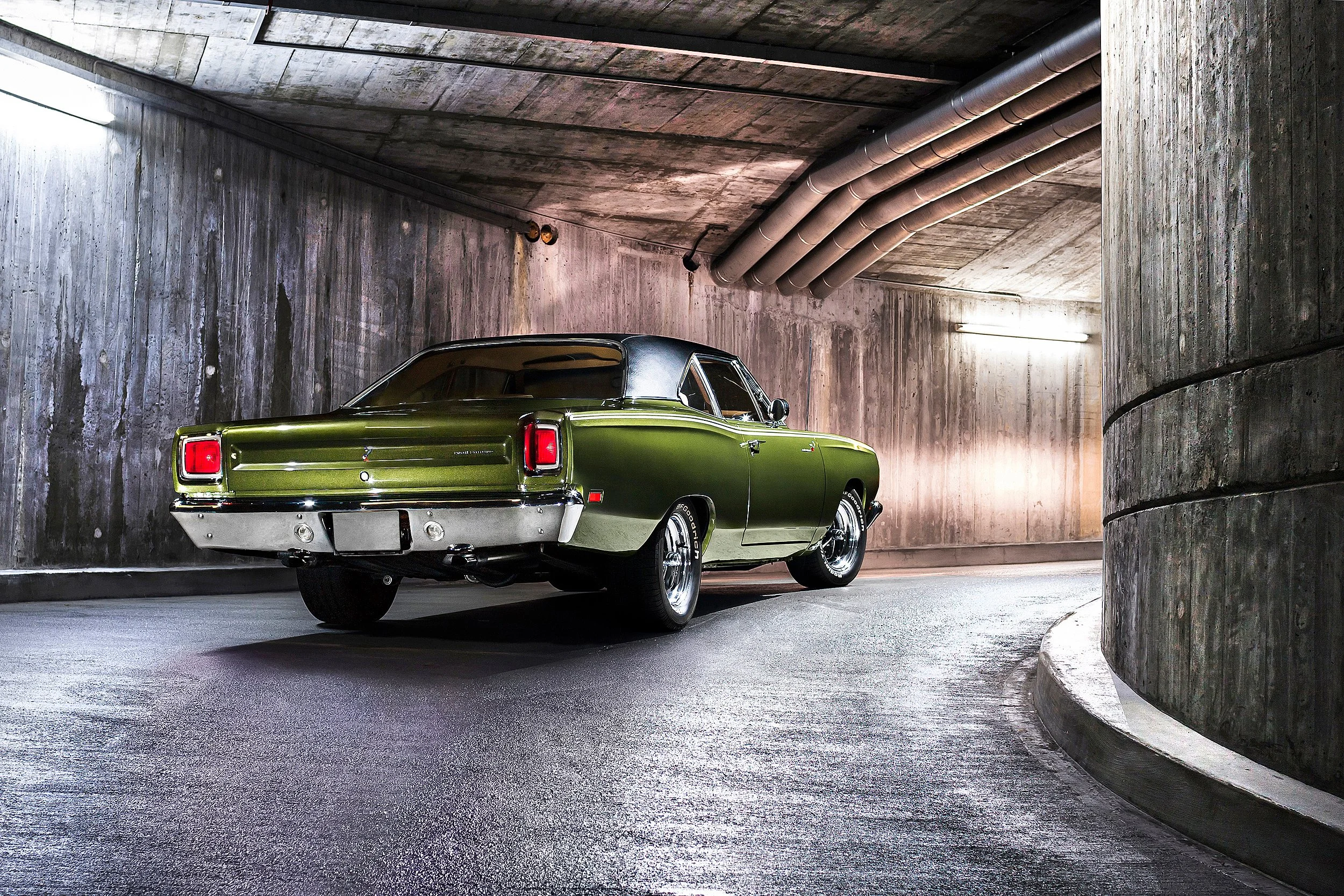 Ein grüner Oldtimer-Pkw in einer unterirdischen Parkgarage mit Betonwänden und -decken, beleuchtet von fluternden Lichtern.