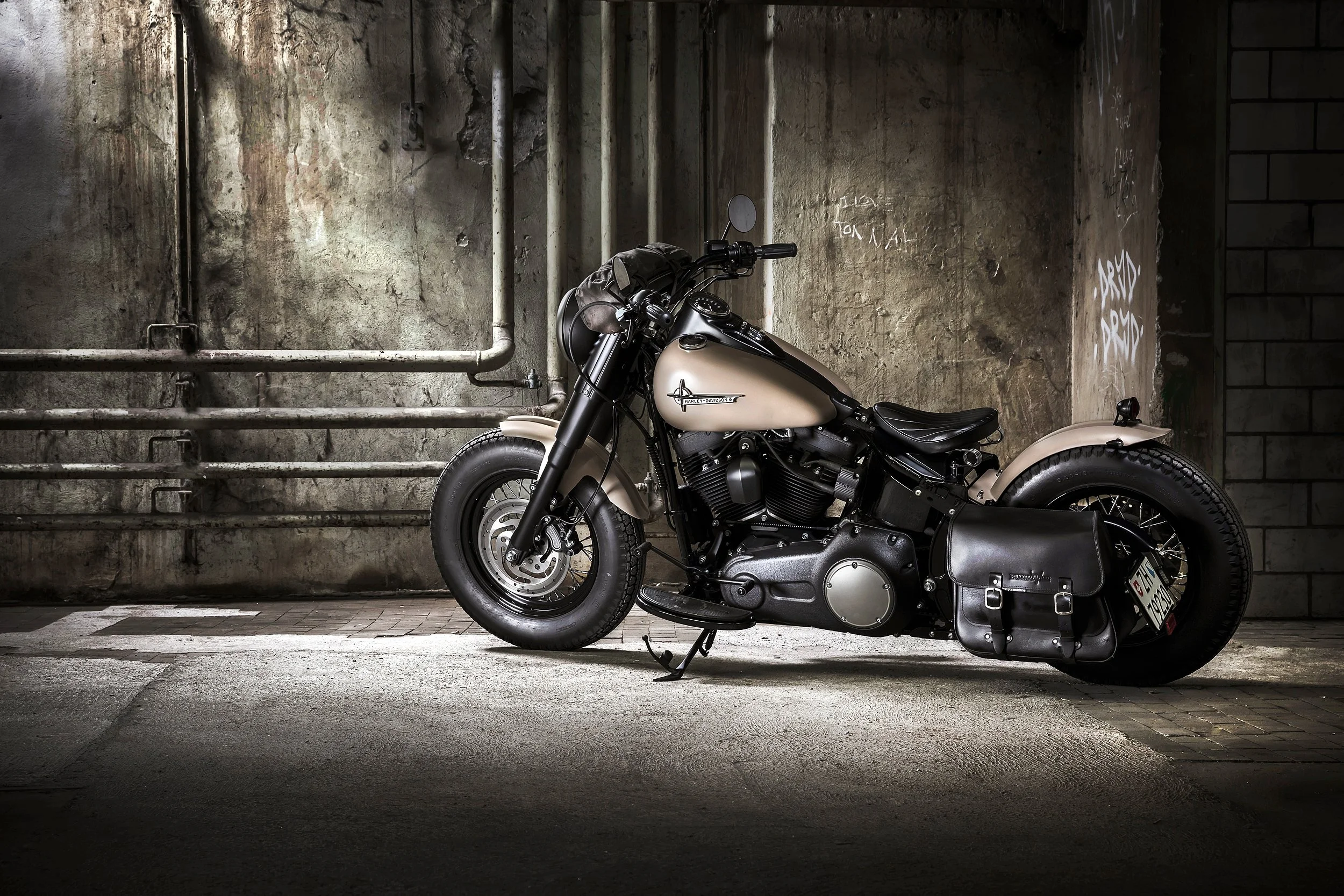 Eine schwarze Harley Davidson Motorräder parkiert vor einer alten, grauen Wand mit Graffiti in einer Tiefgarage.