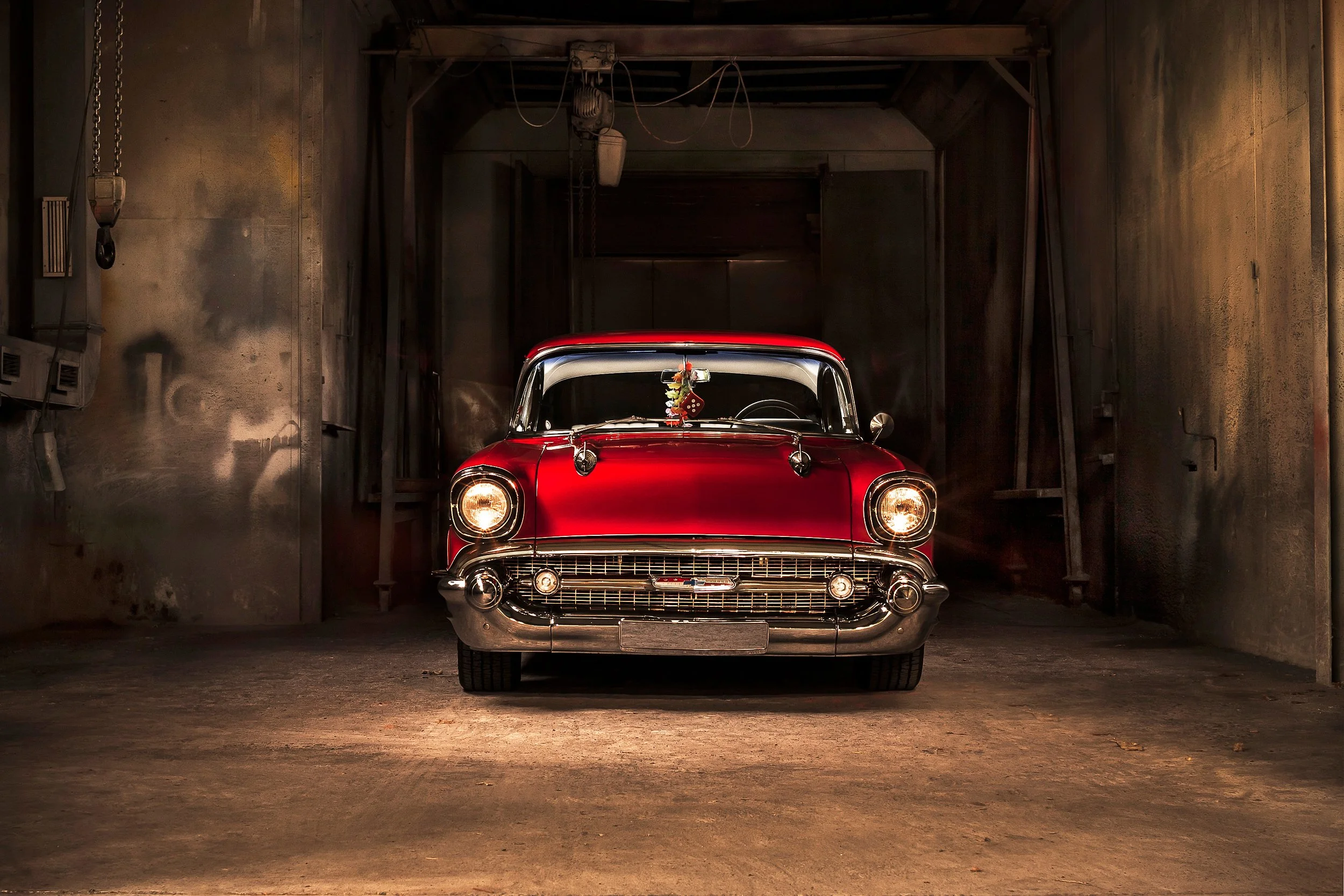 Ein roter Oldtimer steht in einer dunklen Garage, die Wände sind metallisch und abgenutzt.