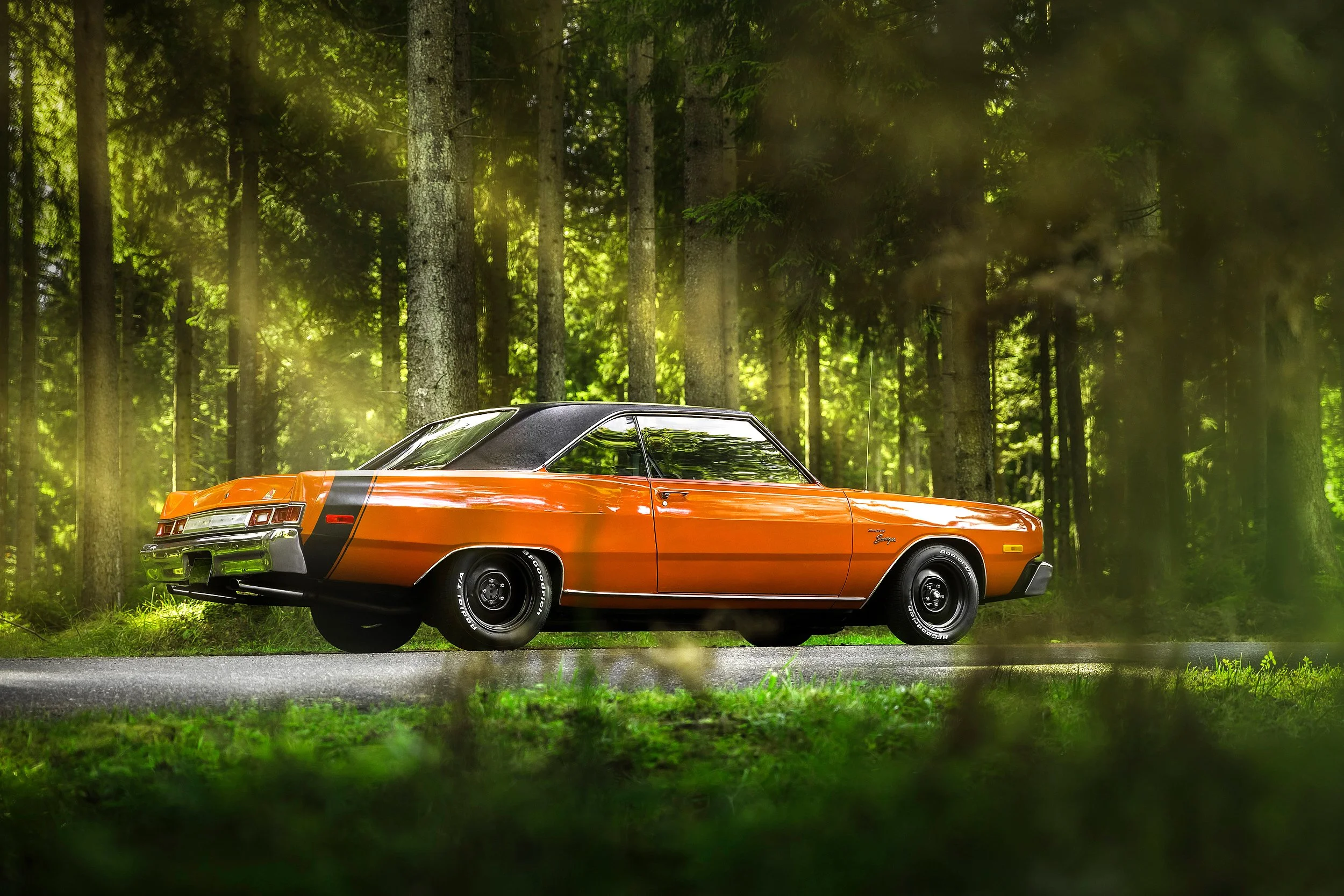 Ein orangefarbener Oldtimer-Auto steht auf einer Straße in einem bewaldeten Gebiet, umgeben von grünen Bäumen und B foliage.