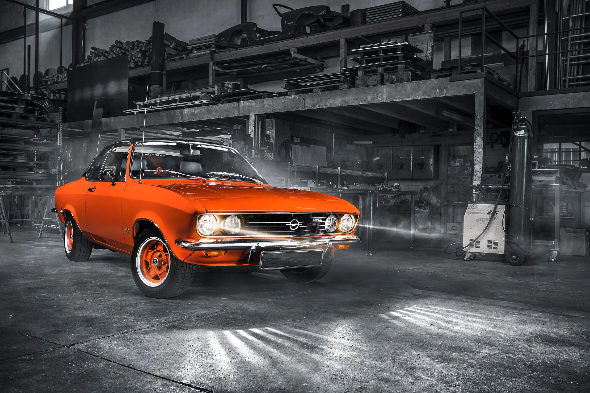 Ein orangefarbener Oldtimer-Auto wird in einer Werkstatt gewartet, umgeben von Werkzeugen und Ausrüstung.