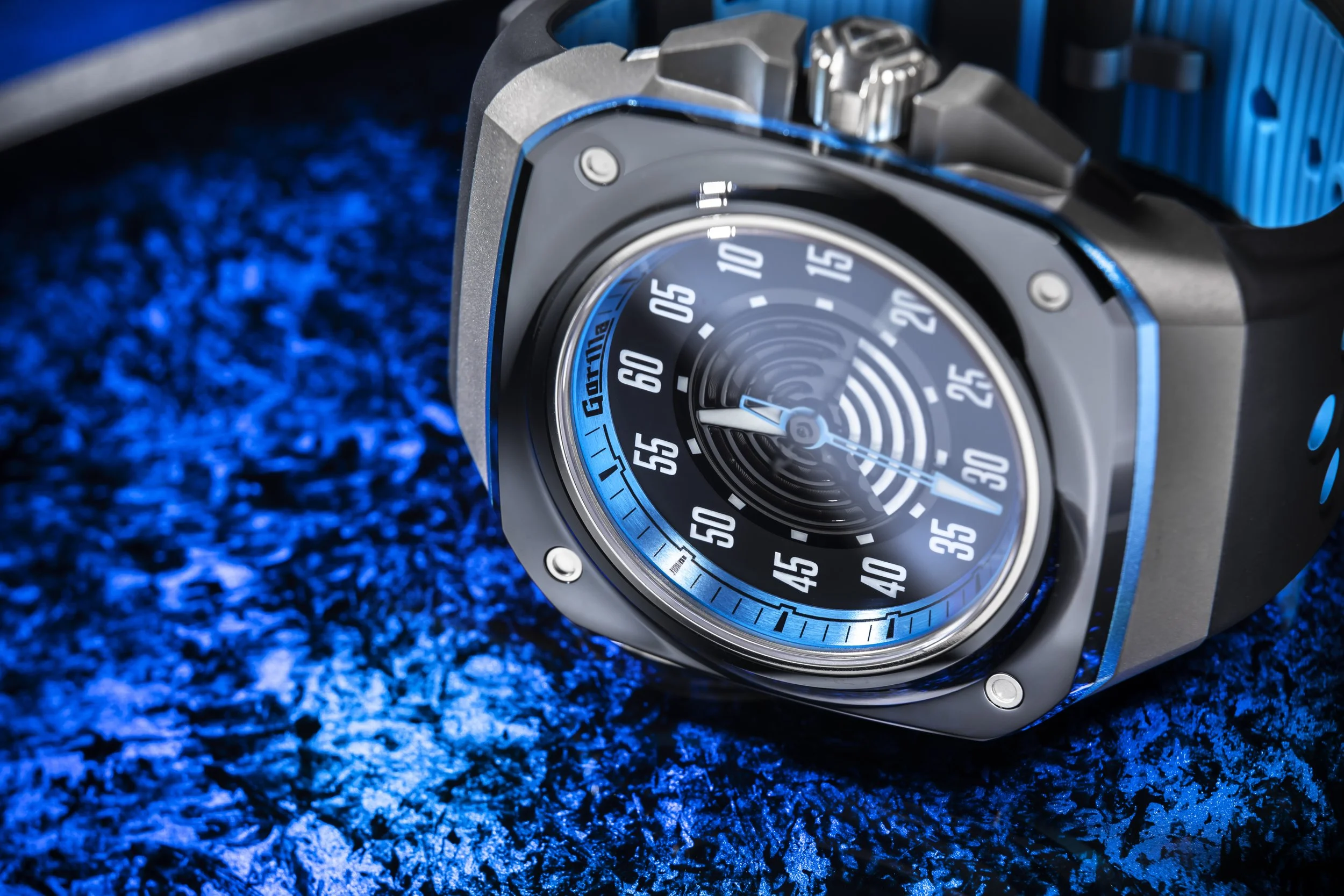 Nahaufnahme einer modernen Armbanduhr mit schwarzem Zifferblatt, blauer Akzentlinie und blauer Zeiger auf einer bläulichen Oberfläche.