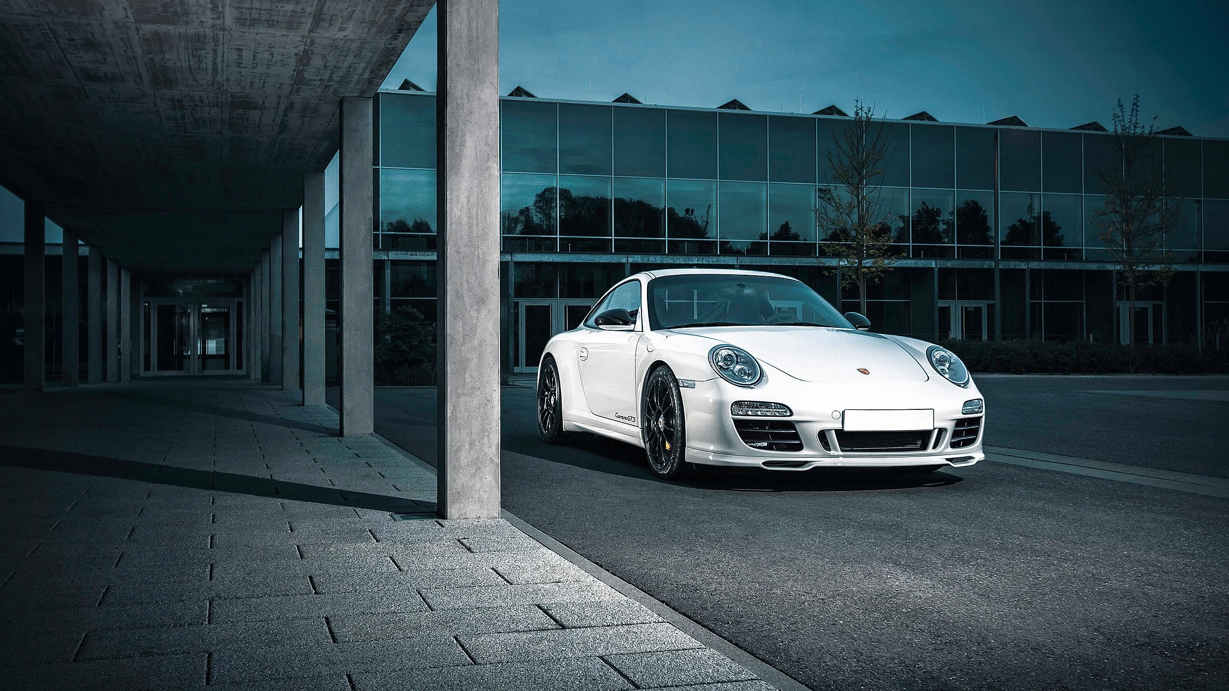 Weiße Porsche Carrera GTS vor einem modernen, gläsernen Gebäude bei Nacht.