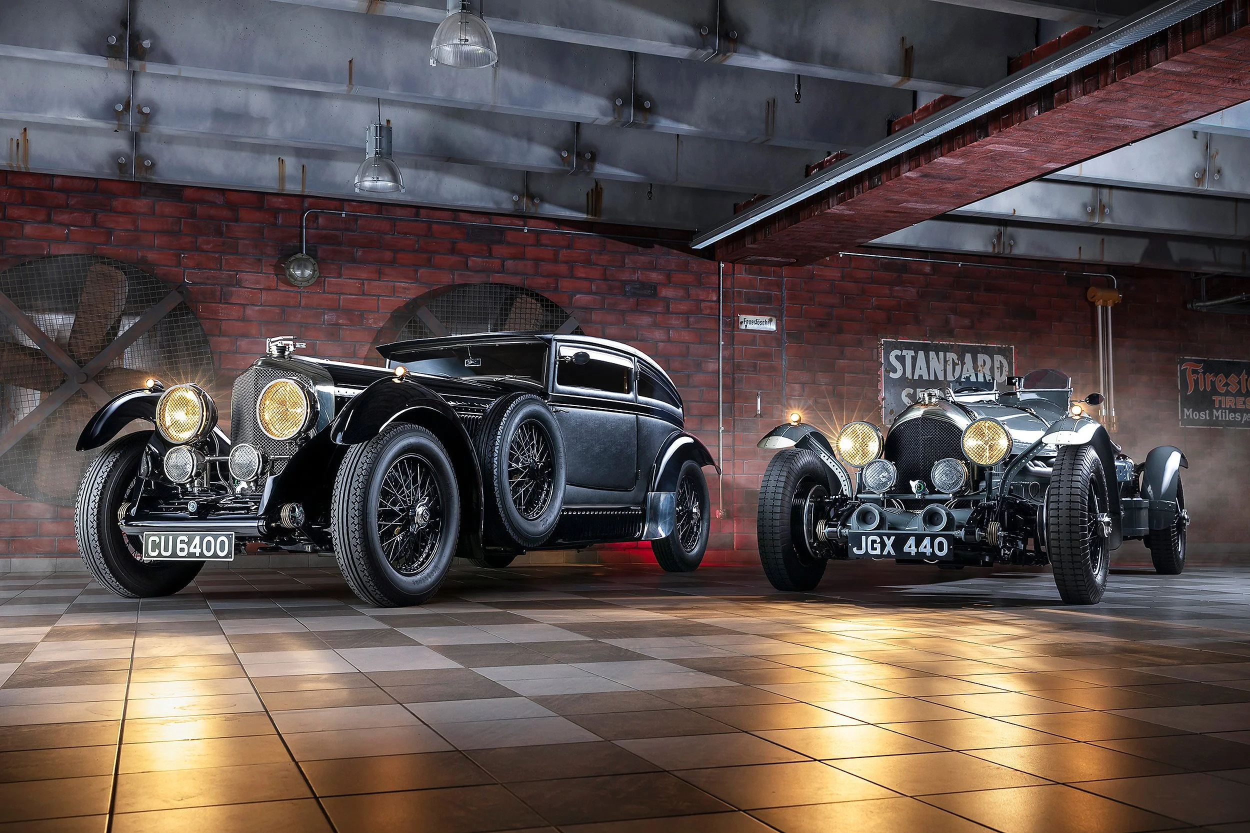 Zwei klassische Autos in einer Werkstatt mit roter Ziegelwand im Hintergrund, Blechdecke und Neonlicht.