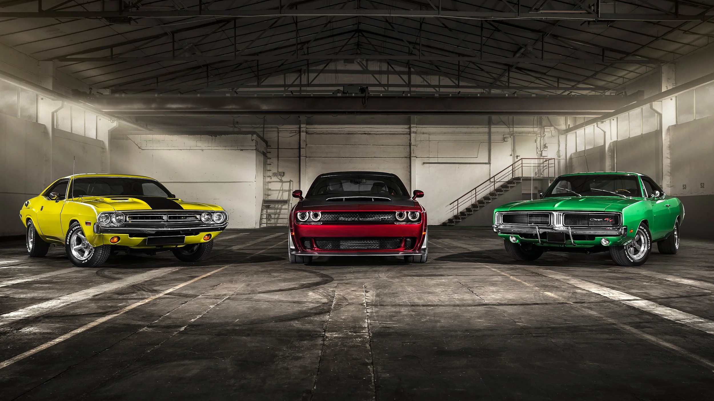 Drei klassische Autos in einer verlassenen Halle, gelb, rot und grün, von vorne fotografiert.