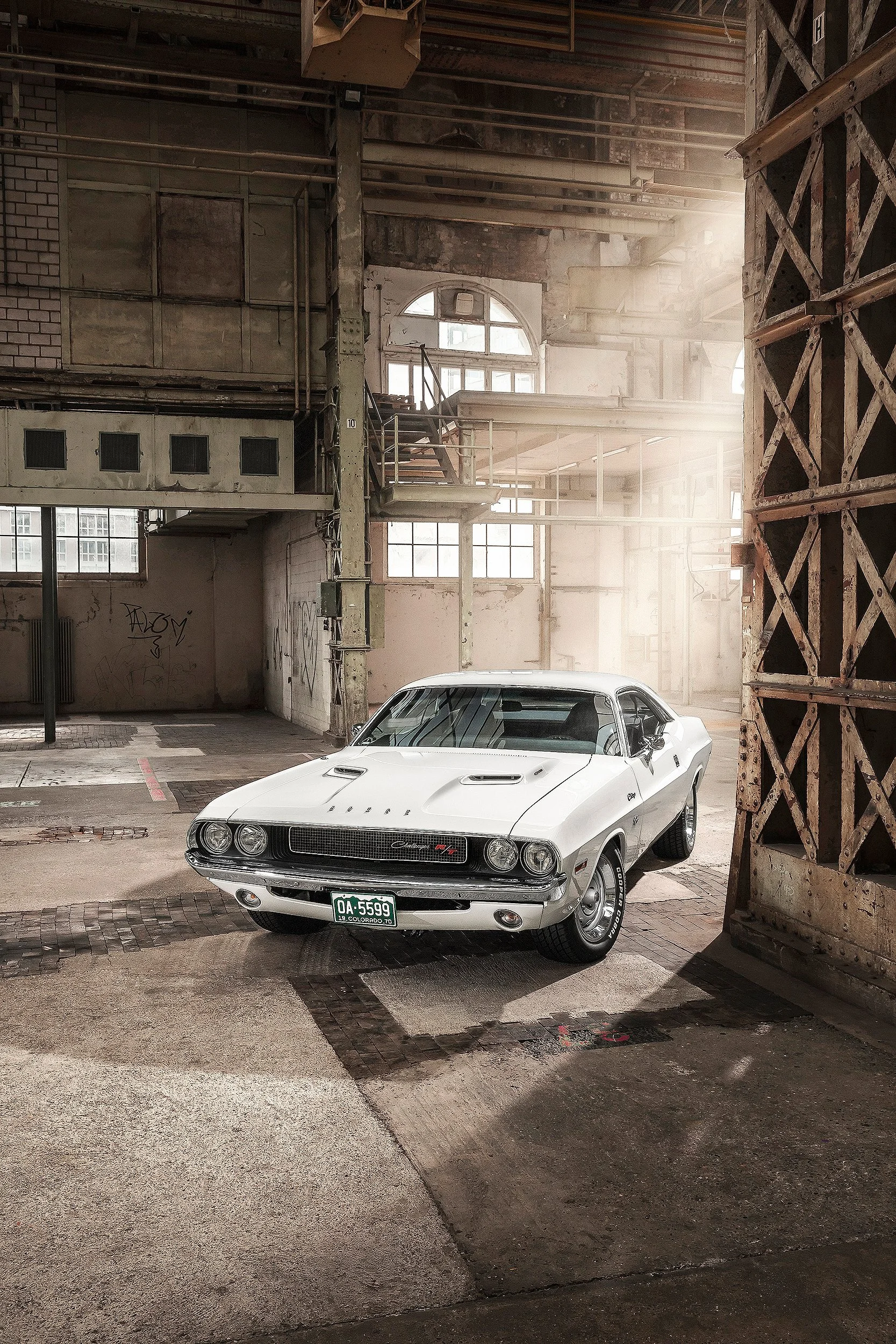 Ein weißer Oldtimer-Auto mit USA-Kennzeichen steht in einem alten, verfallenen Industriegebäude mit hohen Fenstern und rostigen Metallstrukturen.